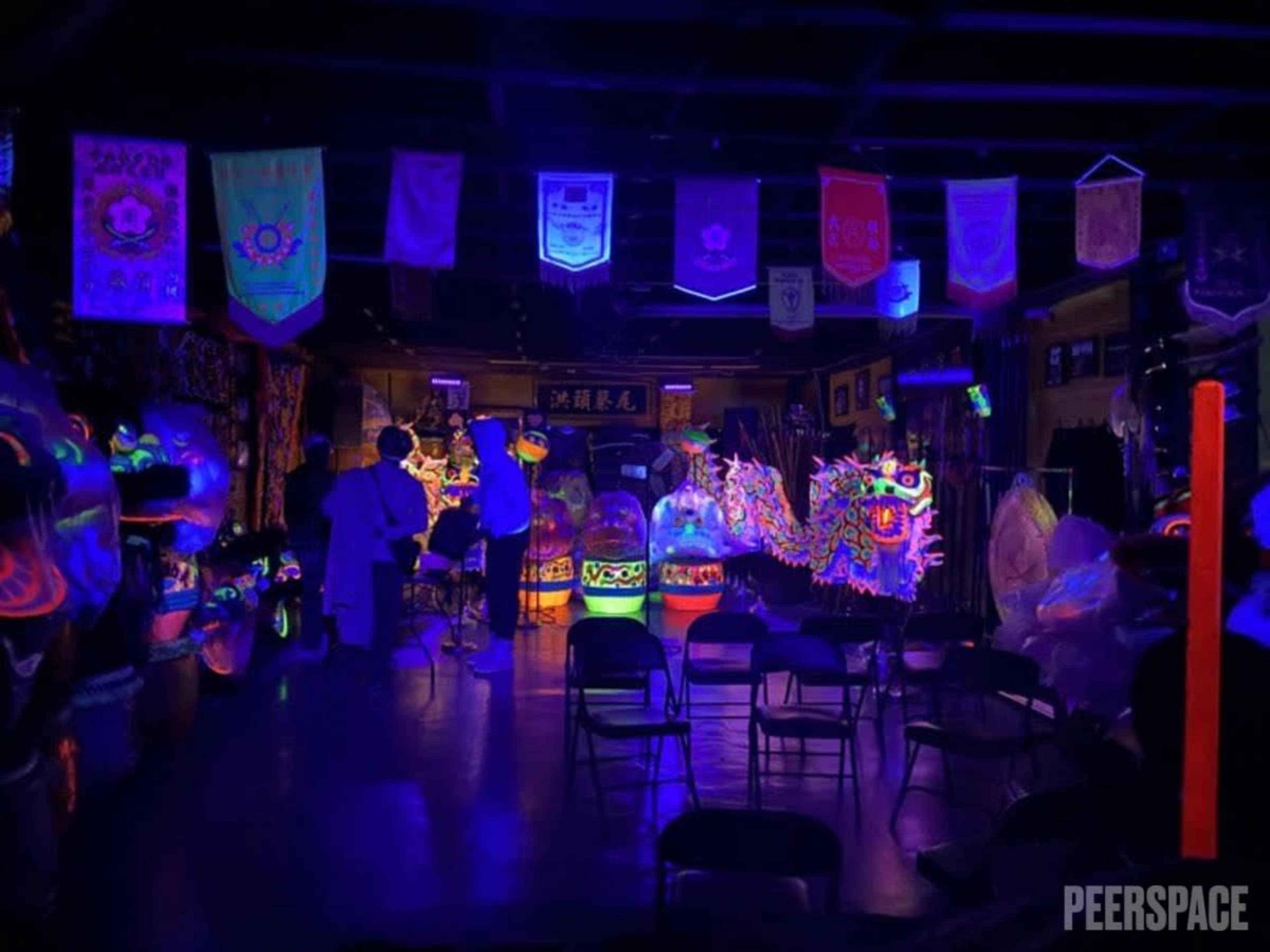 The image shows a dimly lit room decorated with colorful banners and illuminated dragon costumes, set up for a performance or event.