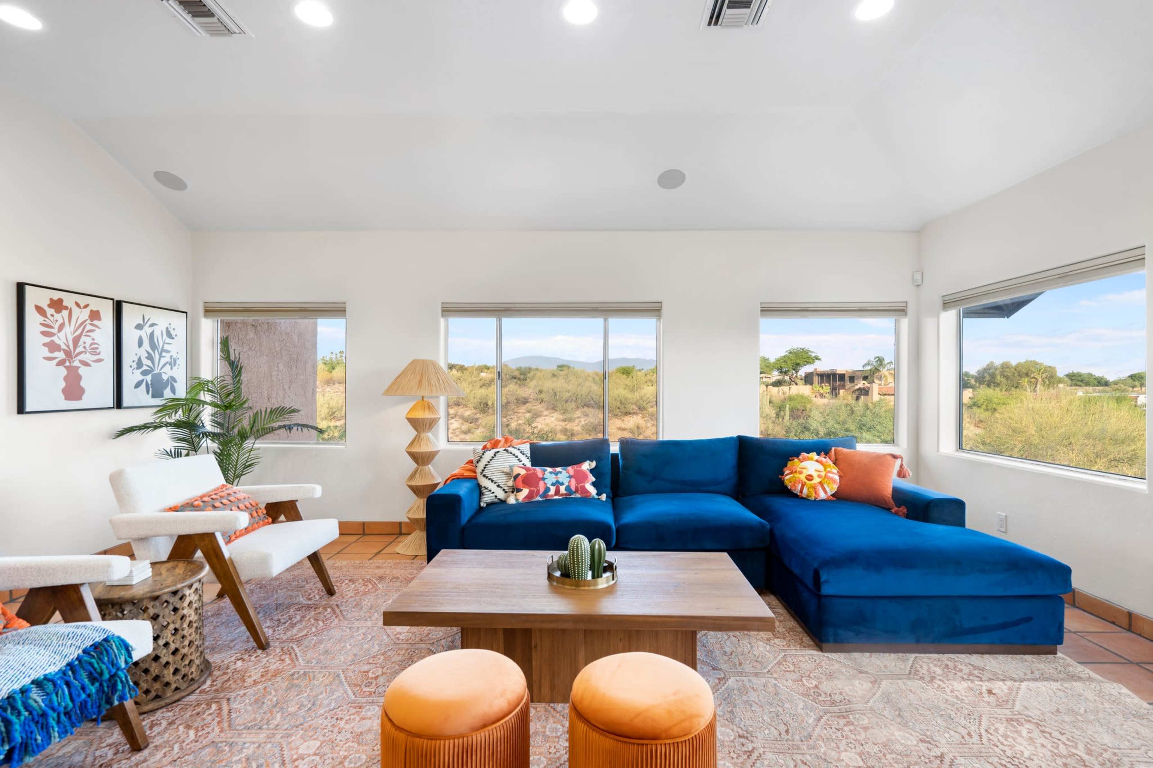 The living room features a blue sectional sofa, a wooden coffee table, and large windows that provide a view of the surrounding landscape.