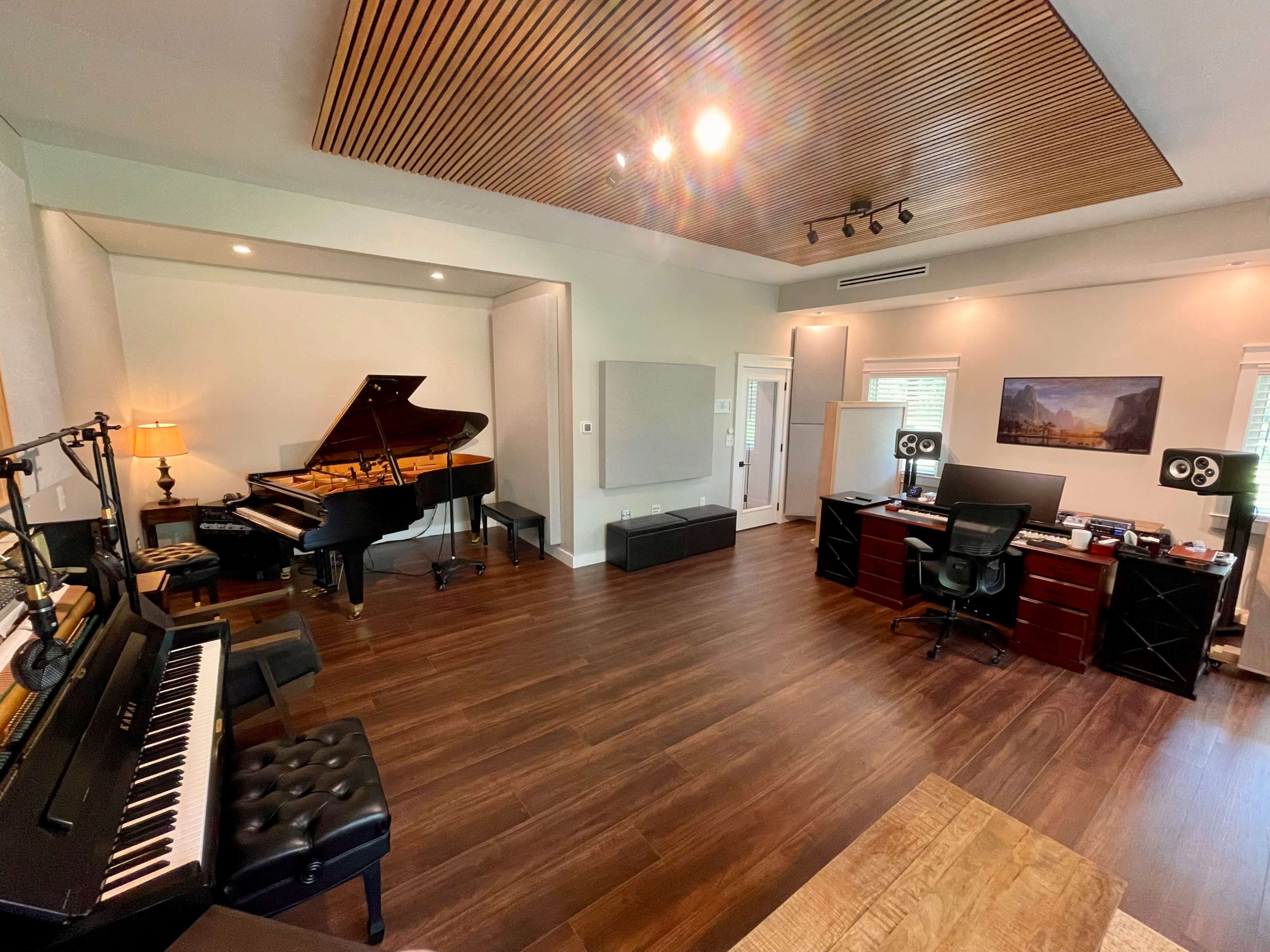 A music studio with a grand piano, a digital keyboard, and a workspace featuring a desk and audio monitors.