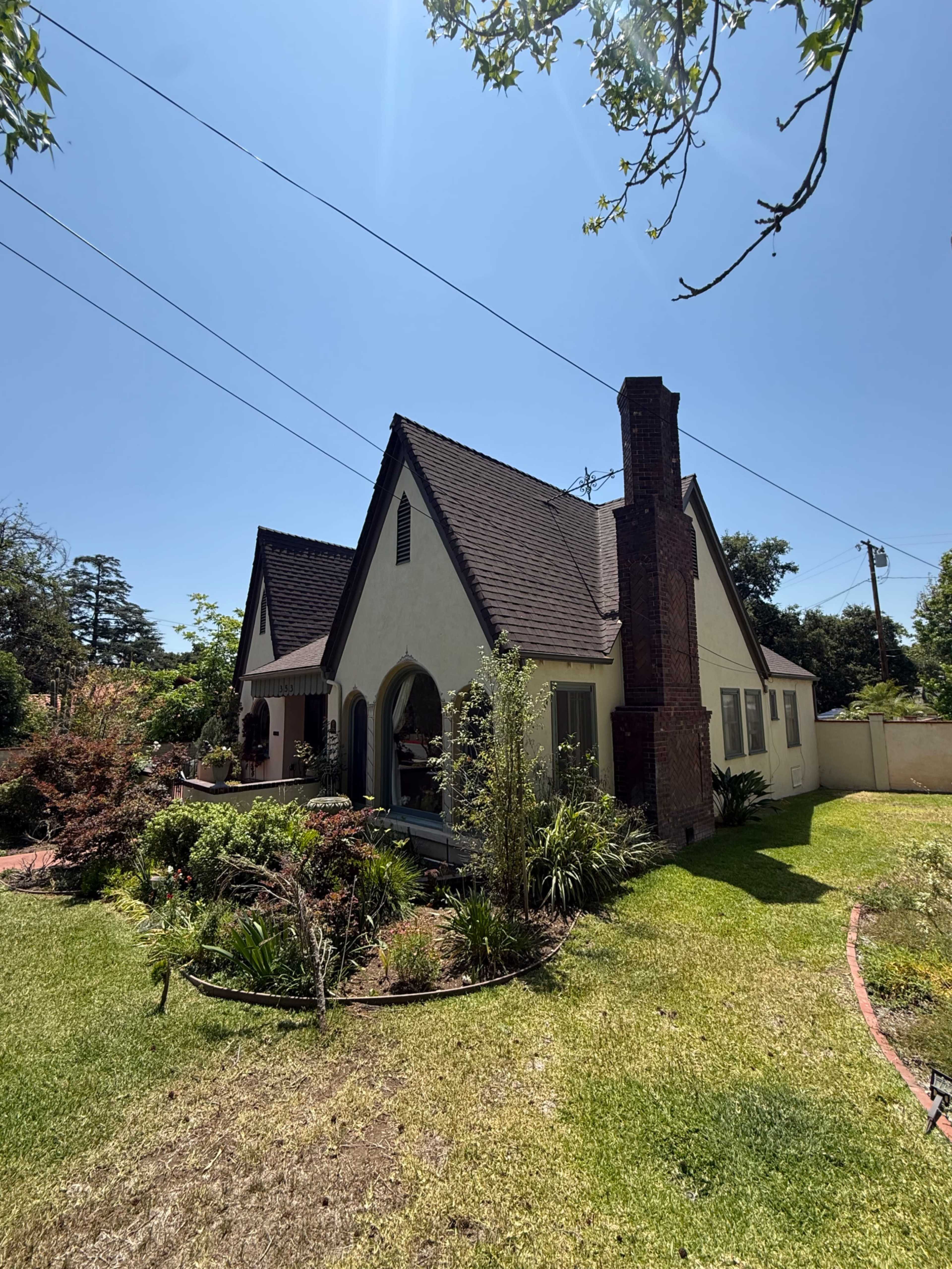 The image shows a charming house with a steeply pitched roof, a brick chimney, and landscaped gardens in the front yard.