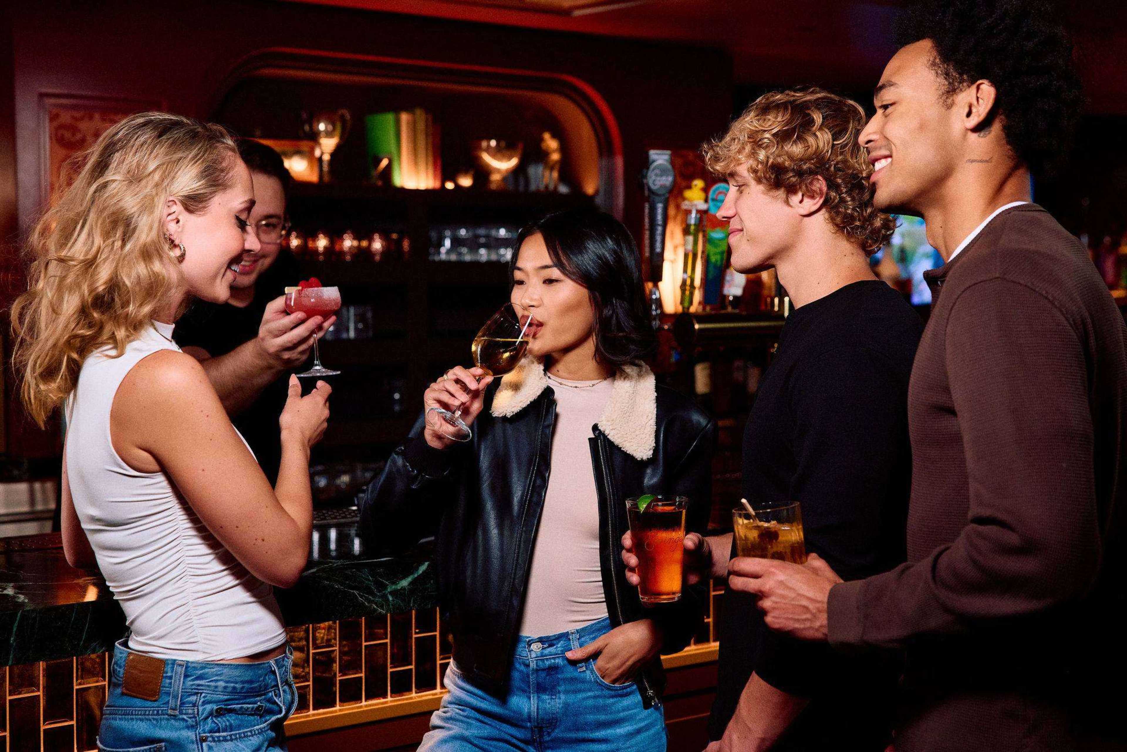 A group of four young adults enjoys drinks at a bar while interacting with each other.