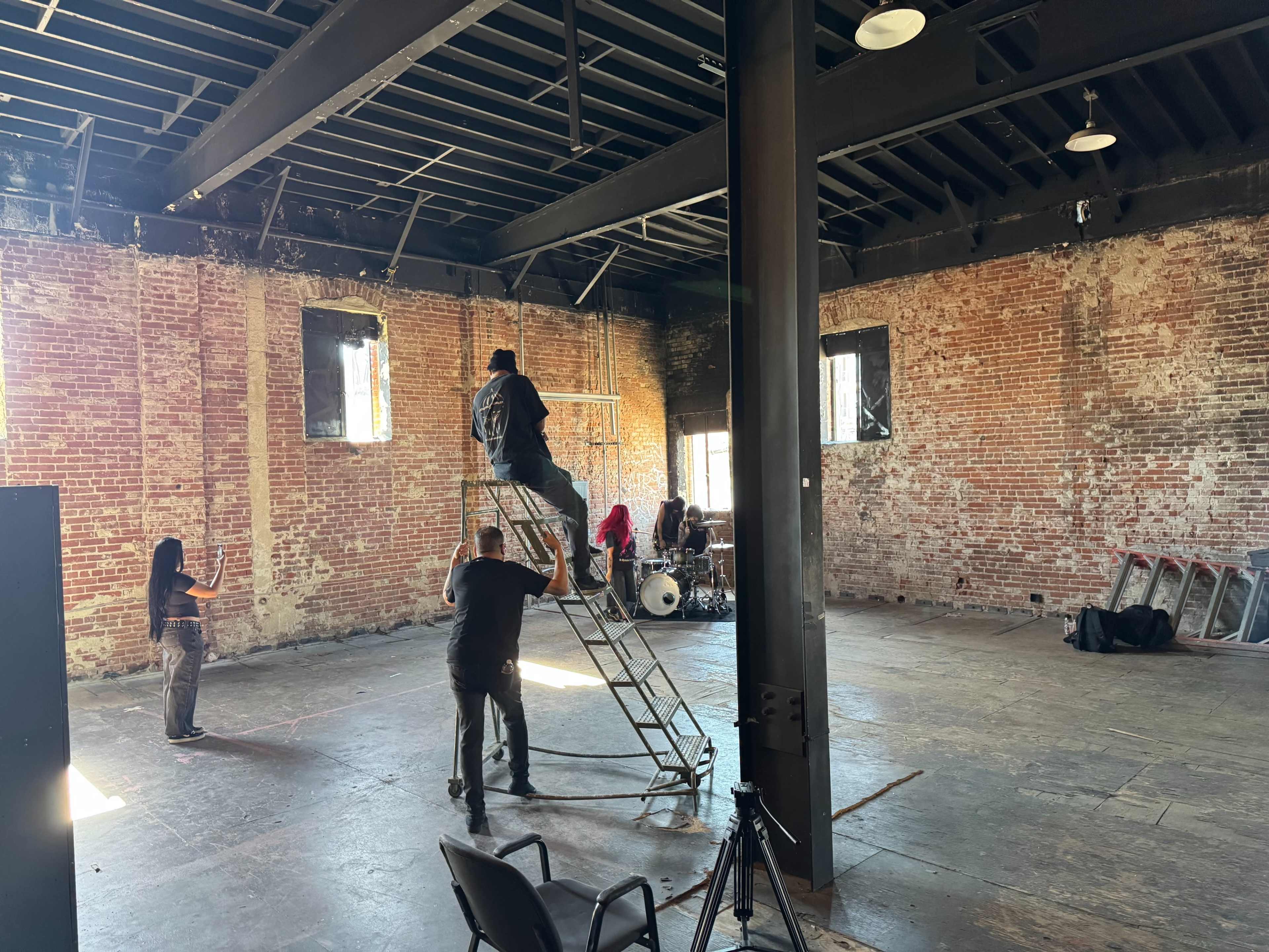 A group of people is setting up a music scene in a large, empty room with exposed brick walls and wooden beams.