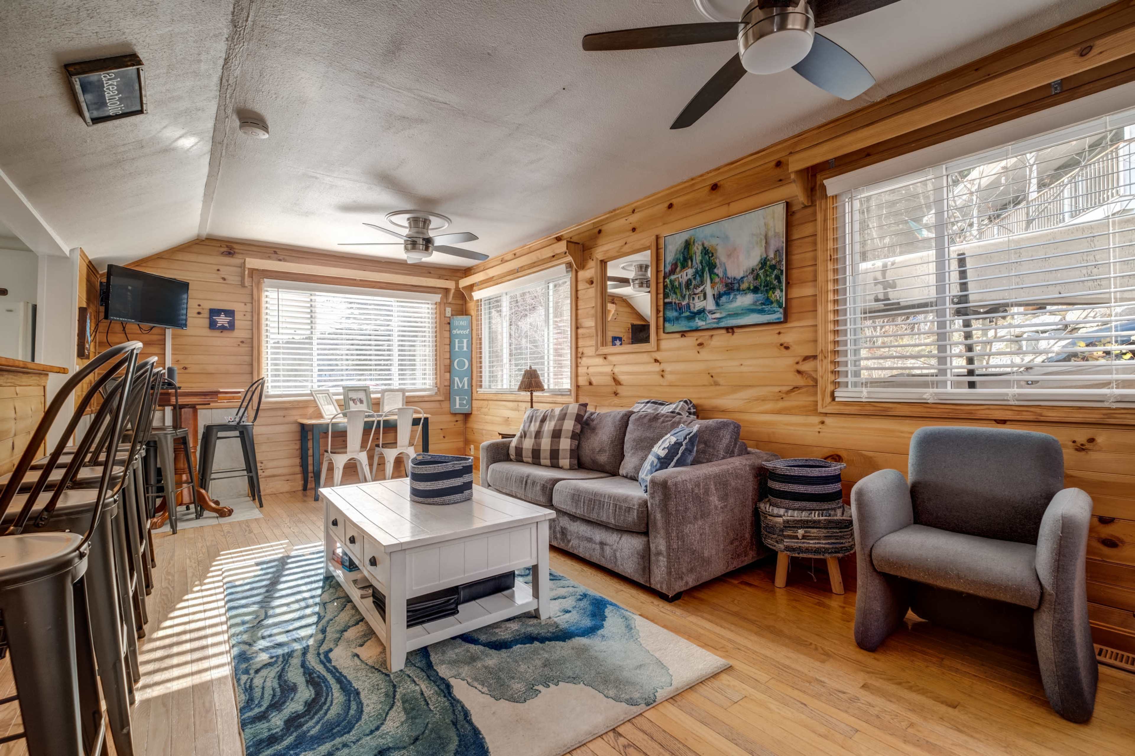 The living room features wooden walls, a sofa, a coffee table, and a dining area with a set of chairs and table beside a window.