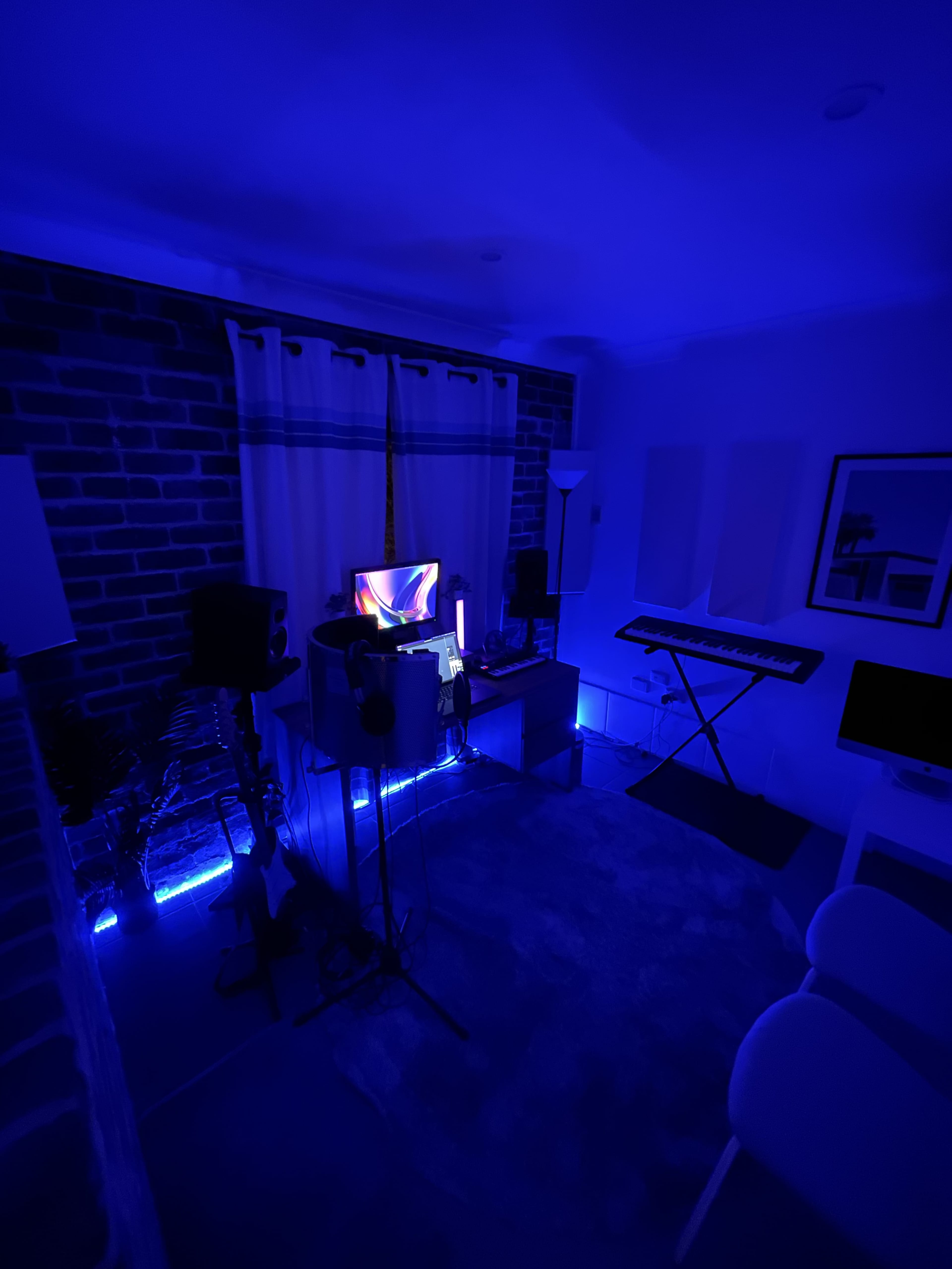 A dimly lit room with blue lighting, featuring music equipment, a computer, and a keyboard against a brick wall.