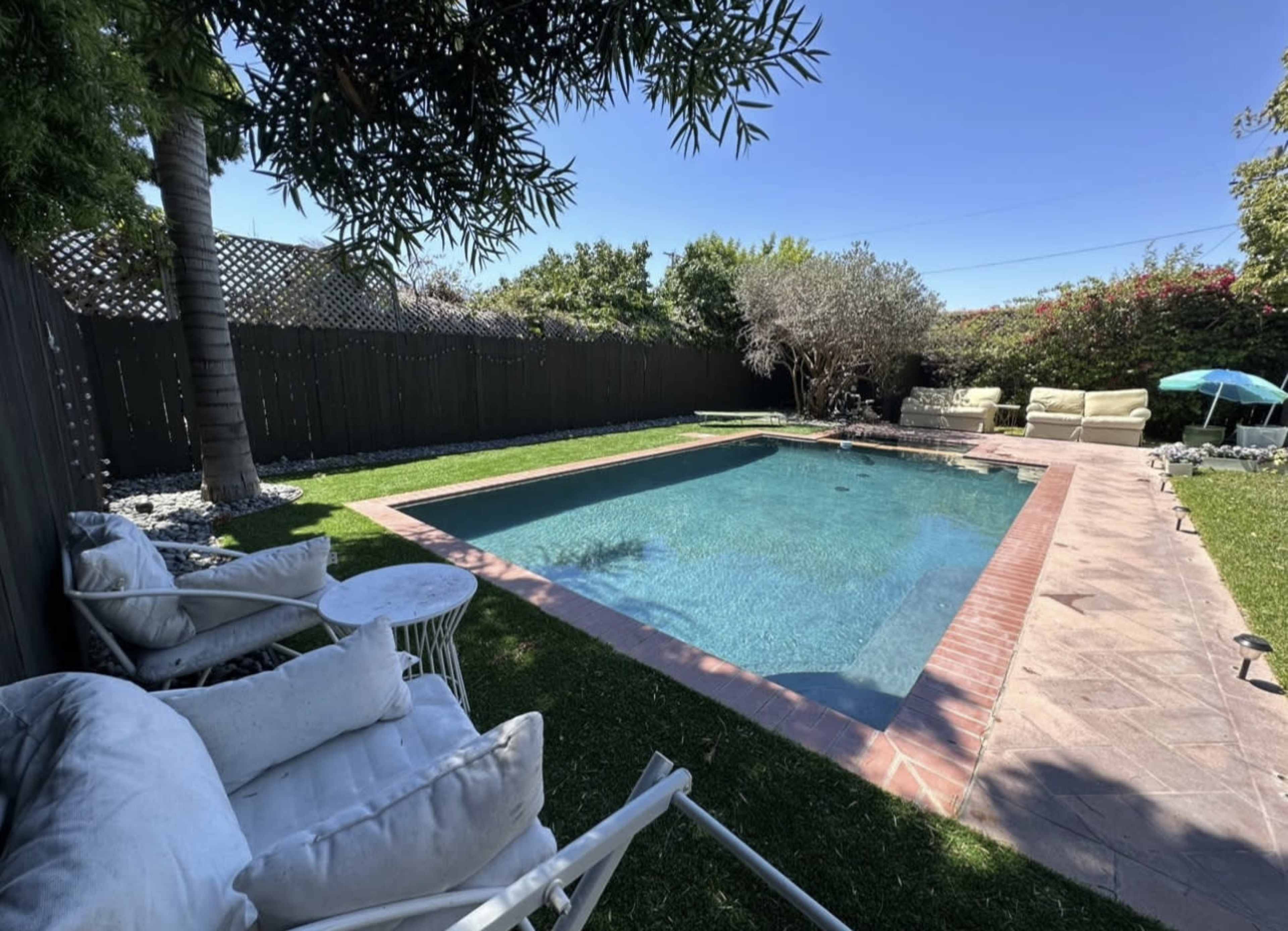 A swimming pool surrounded by a grassy area, with lounge chairs and a small table nearby.