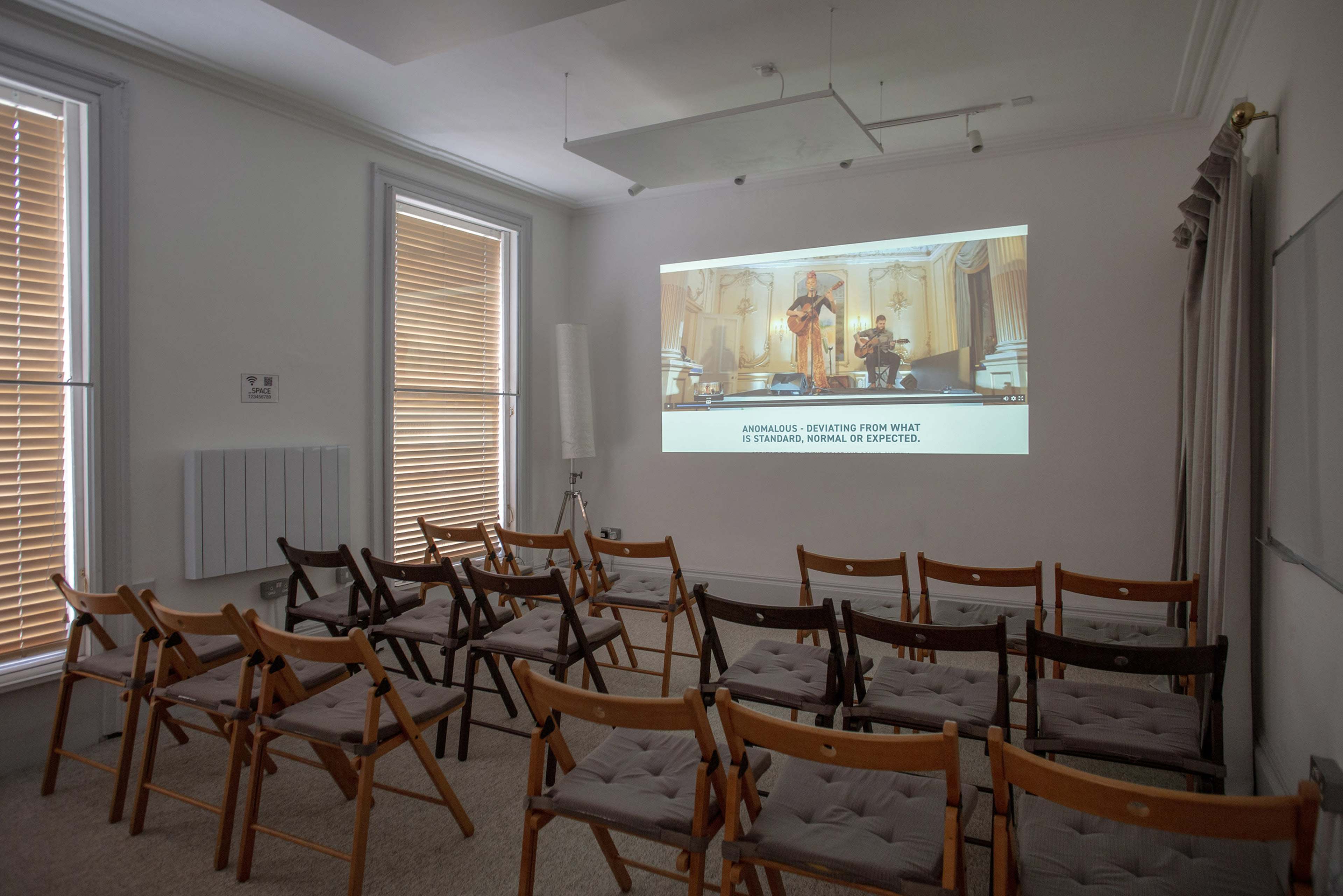 A small room is set up with rows of folding chairs facing a projector screen displaying an image from a presentation.
