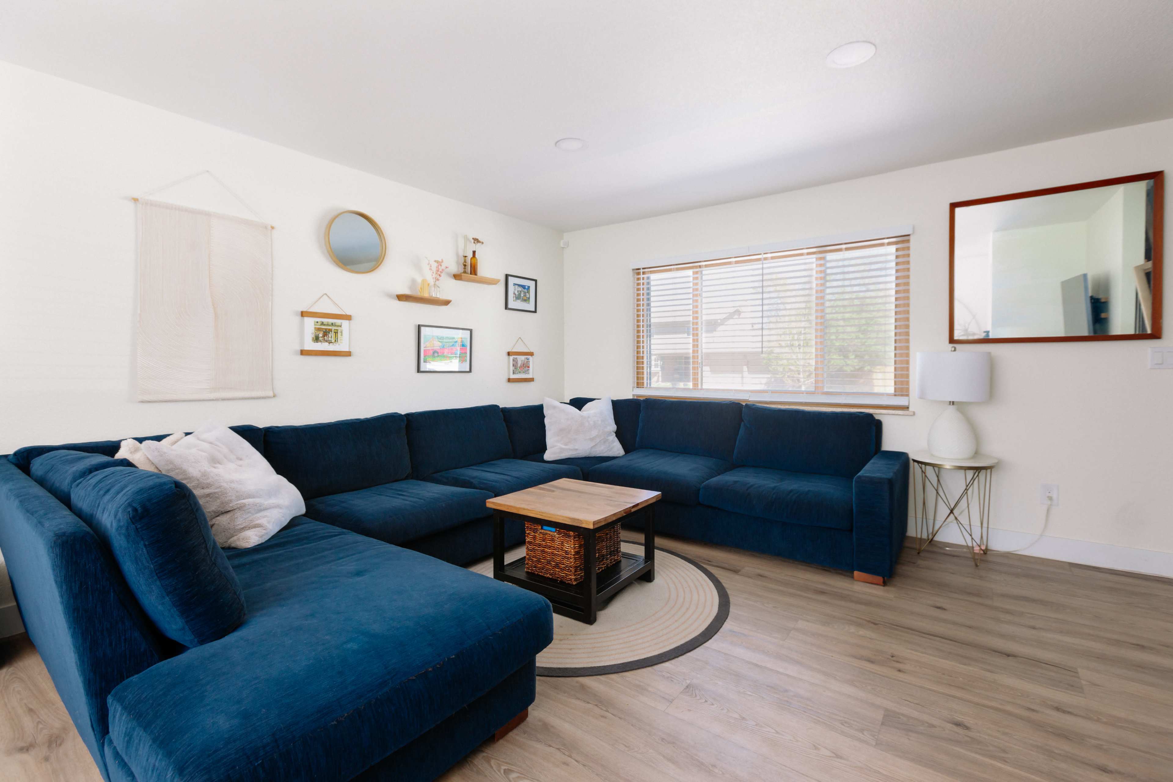 A modern living room with a large blue sectional sofa, a wooden coffee table, and framed artwork on the walls.