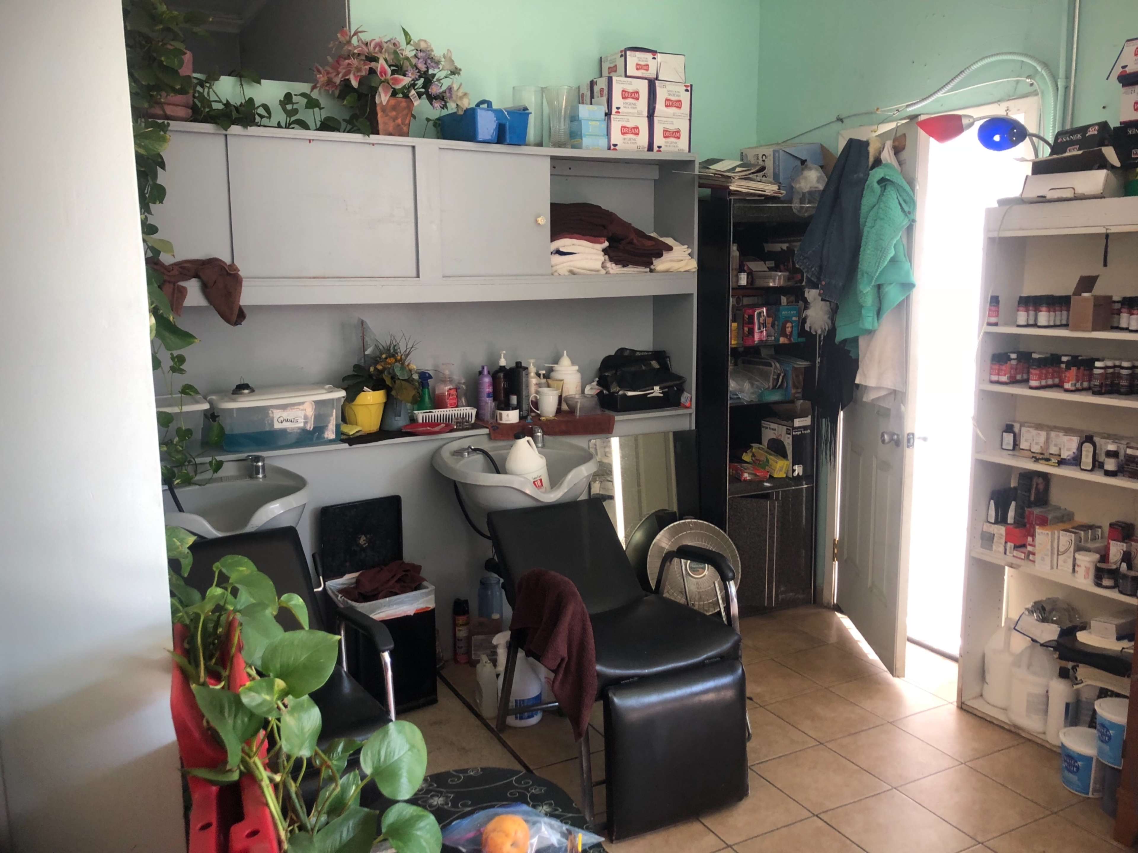 A small salon space with a sink area, two salon chairs, and shelves filled with various products and supplies.