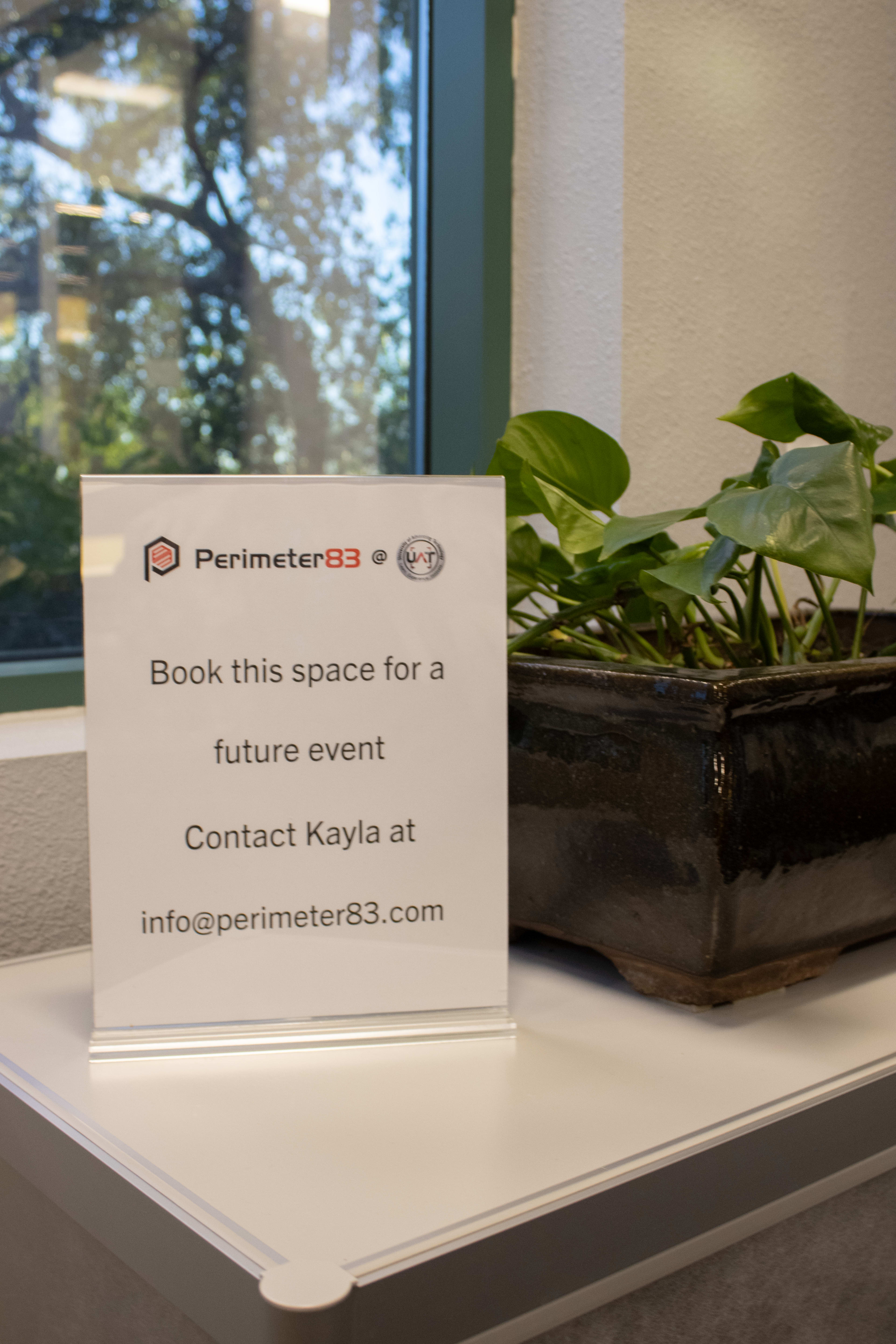 A sign in front of a plant pot invites visitors to book a space for a future event and provides contact information for Kayla.
