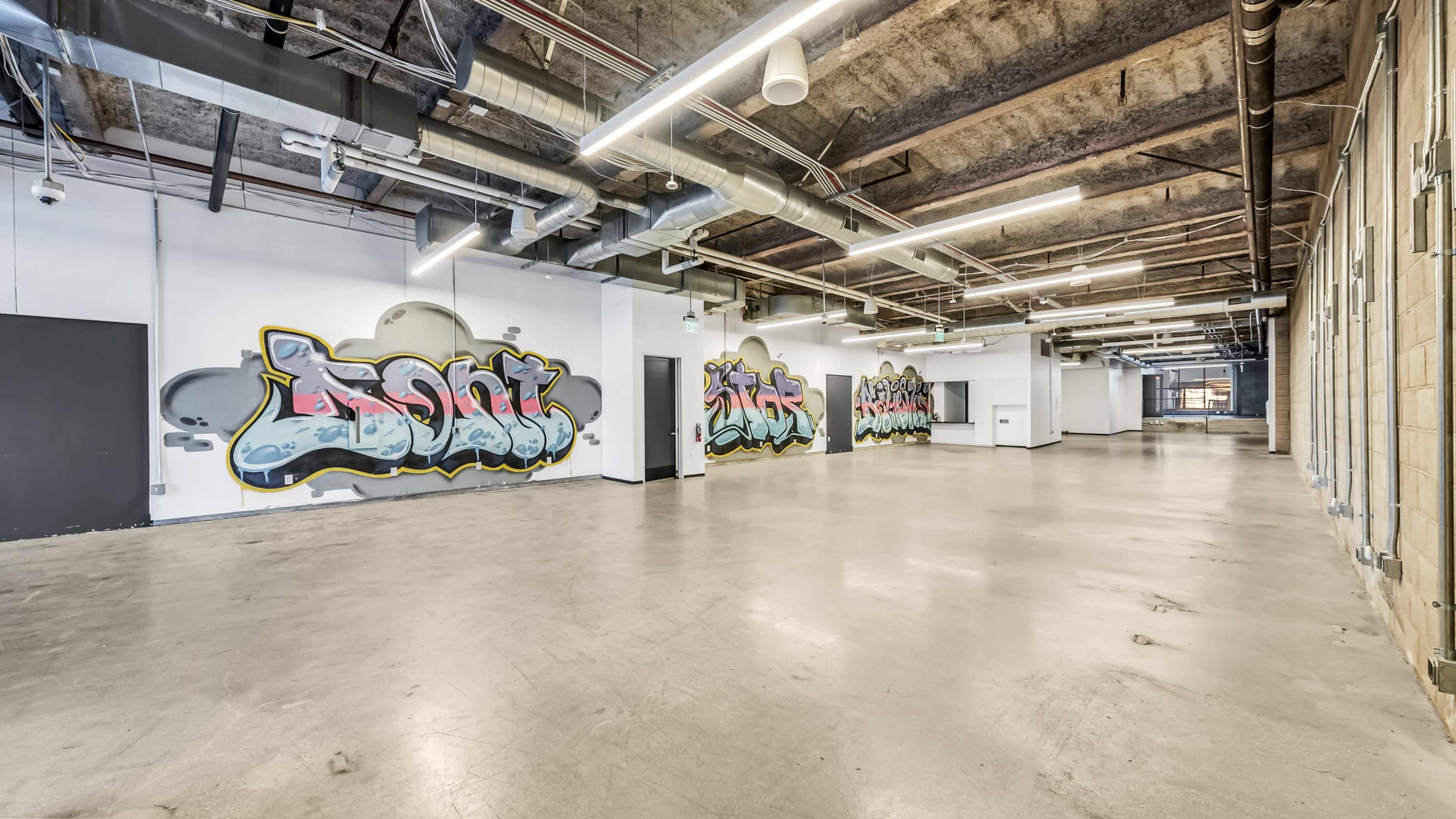 A large, open industrial space with concrete flooring and graffiti-covered walls.