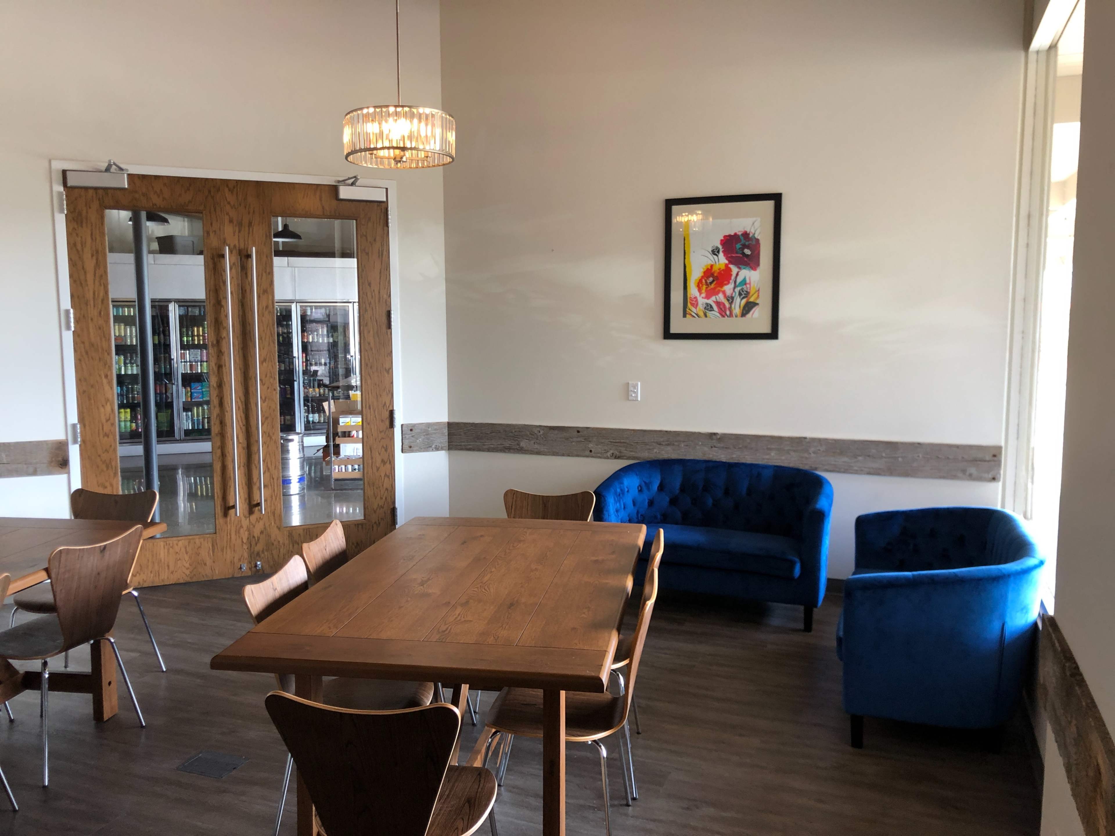 A bright seating area features a wooden table surrounded by chairs, blue velvet couches, and a framed floral artwork on the wall.
