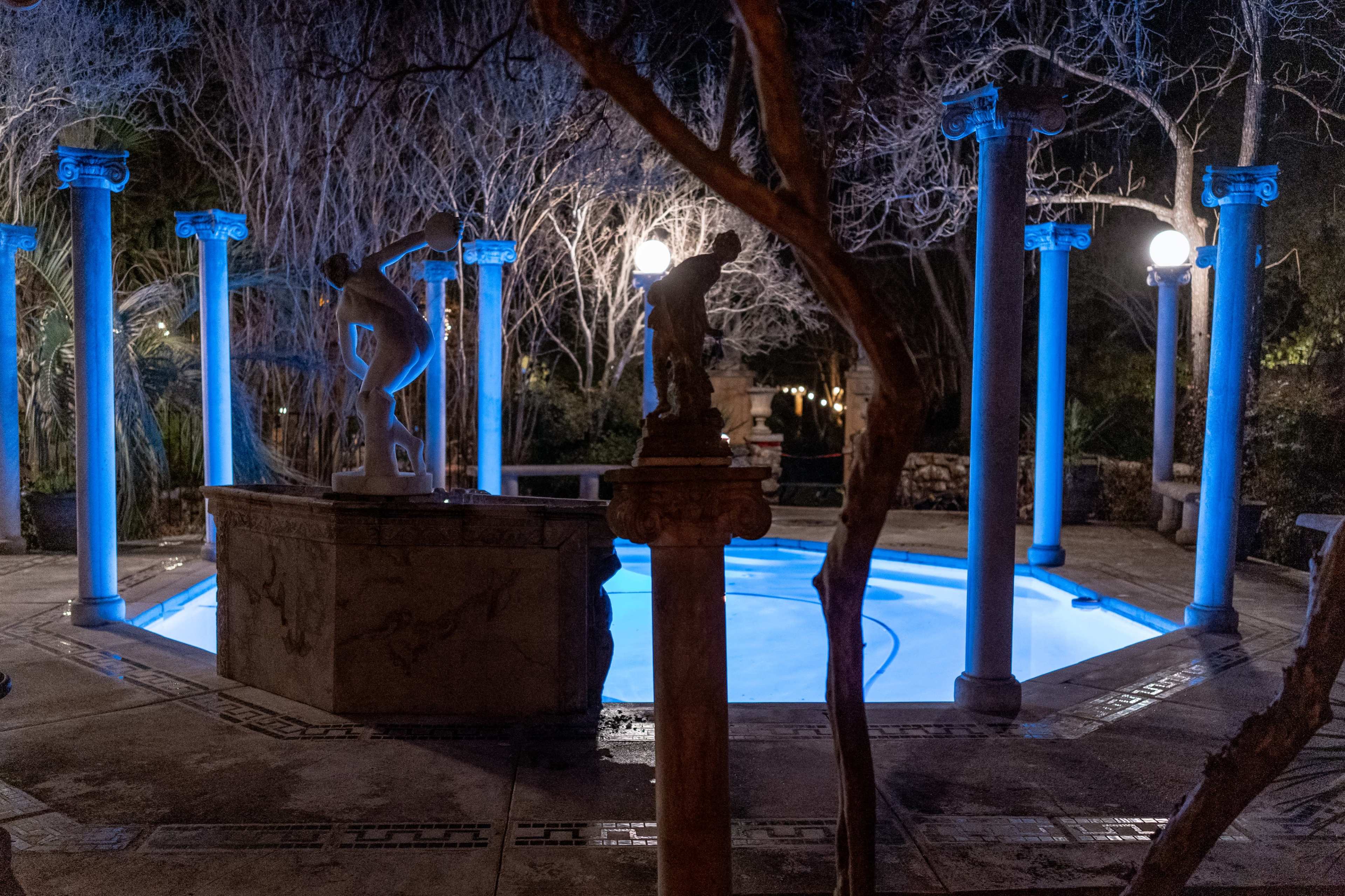 A illuminated circular pool surrounded by columns, with sculptures and dim lighting in a tranquil nighttime setting.