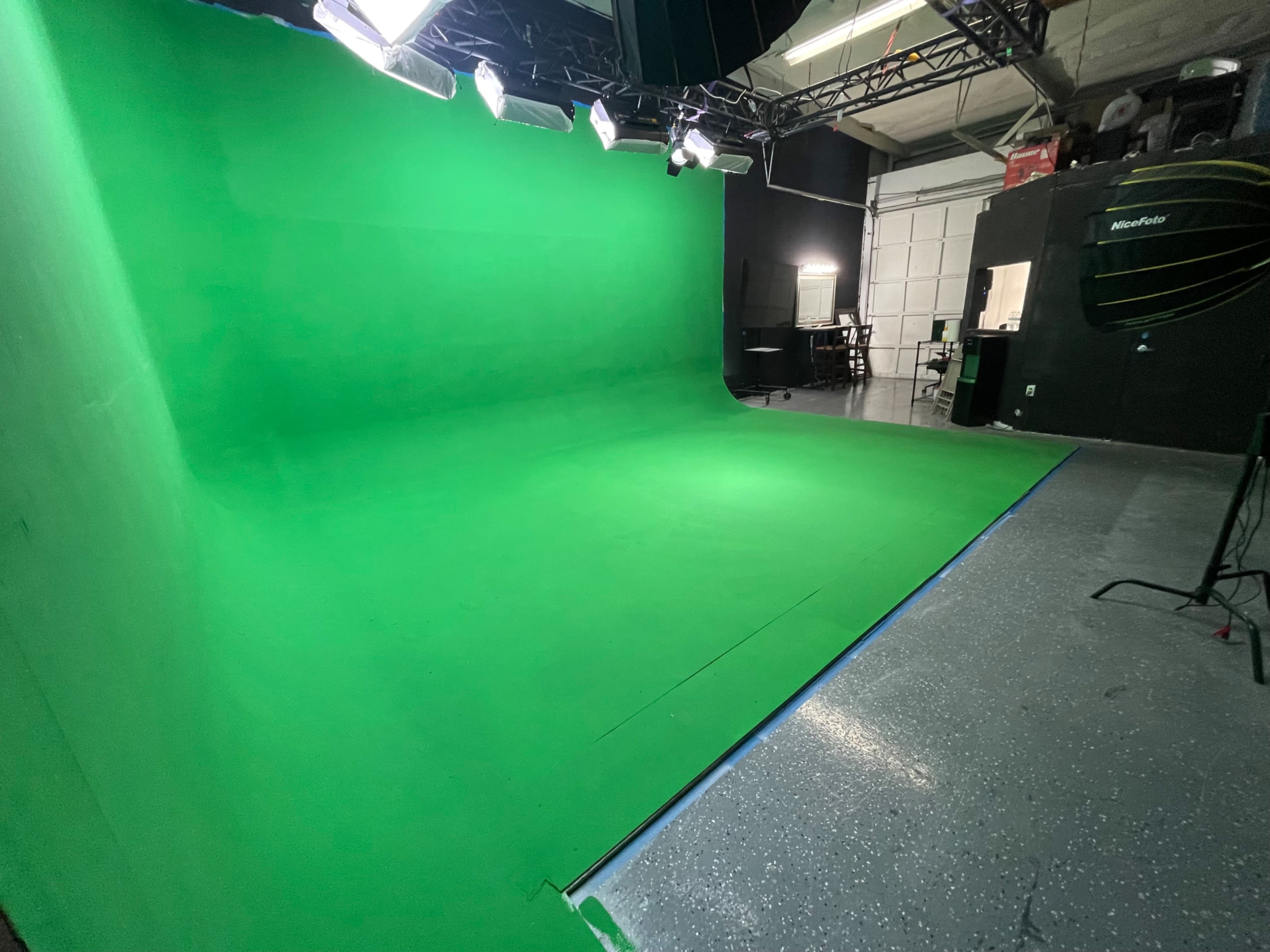 The image shows an empty green screen studio with overhead lights and a polished floor.