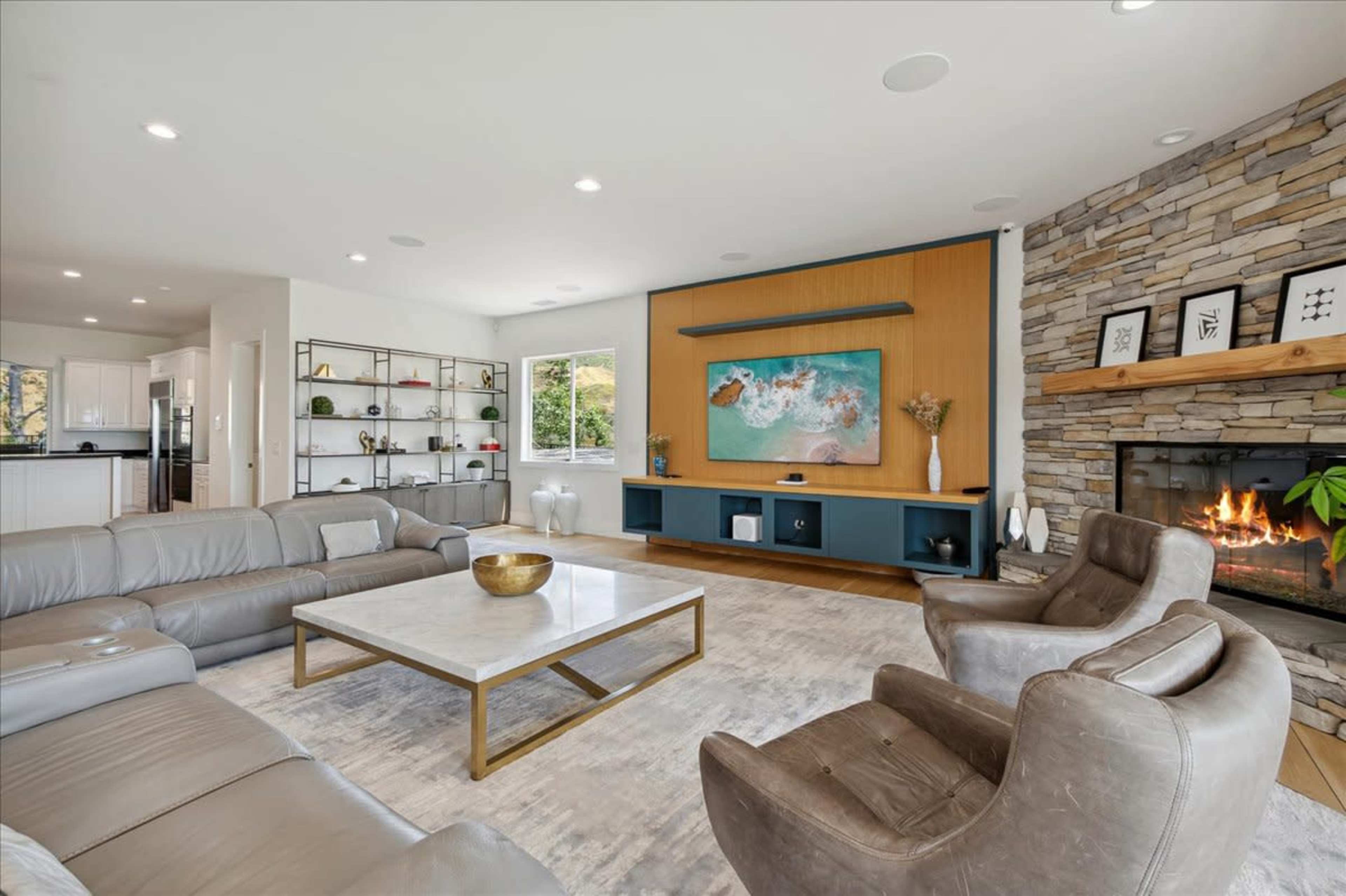 The image shows a modern living room with a stone fireplace, a large sectional sofa, a coffee table, and a stylish wall-mounted television.