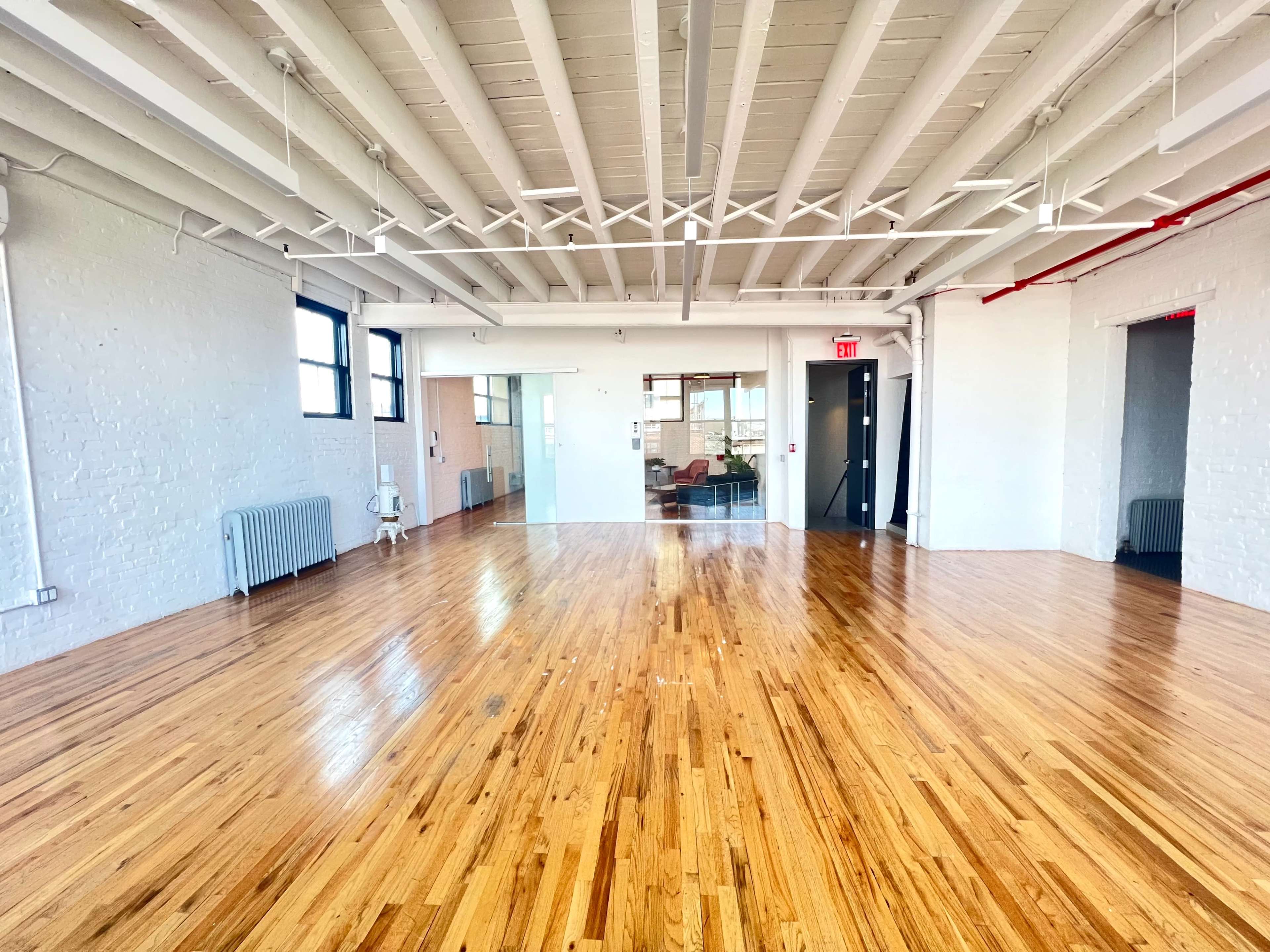 A spacious, empty room with polished wooden floors, white walls, and exposed beams.