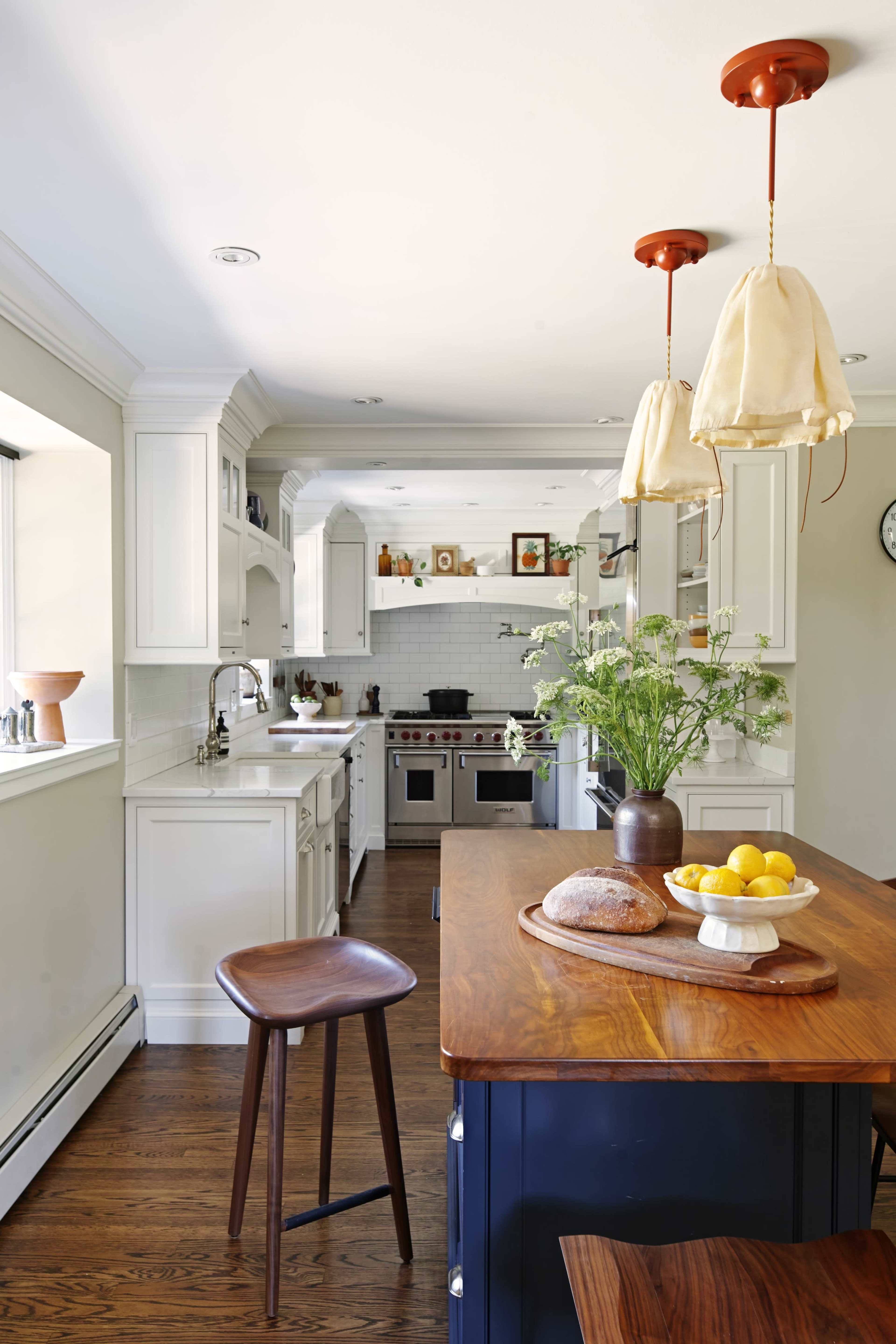 The kitchen features white cabinetry, a wooden island with a bowl of lemons and bread, and pendant lights hanging above.