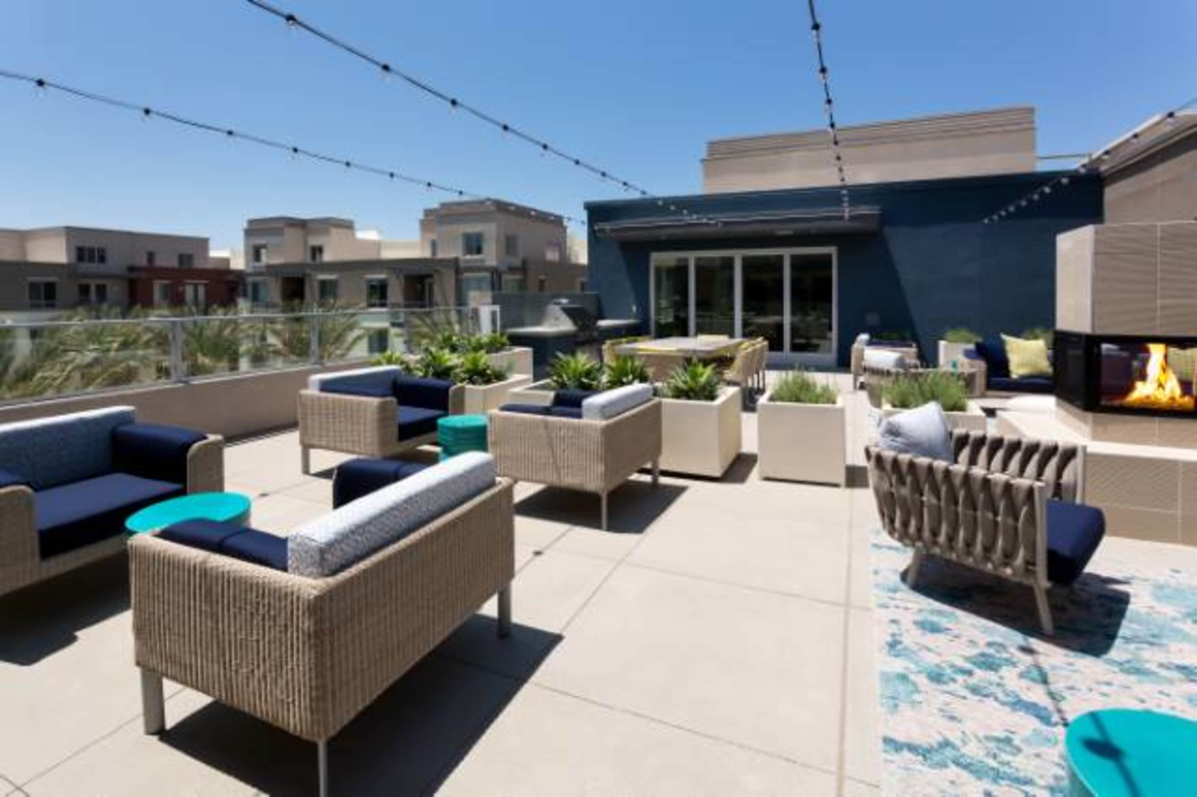 A spacious rooftop area features modern seating arrangements, decorative plants, and an outdoor fireplace under string lights.