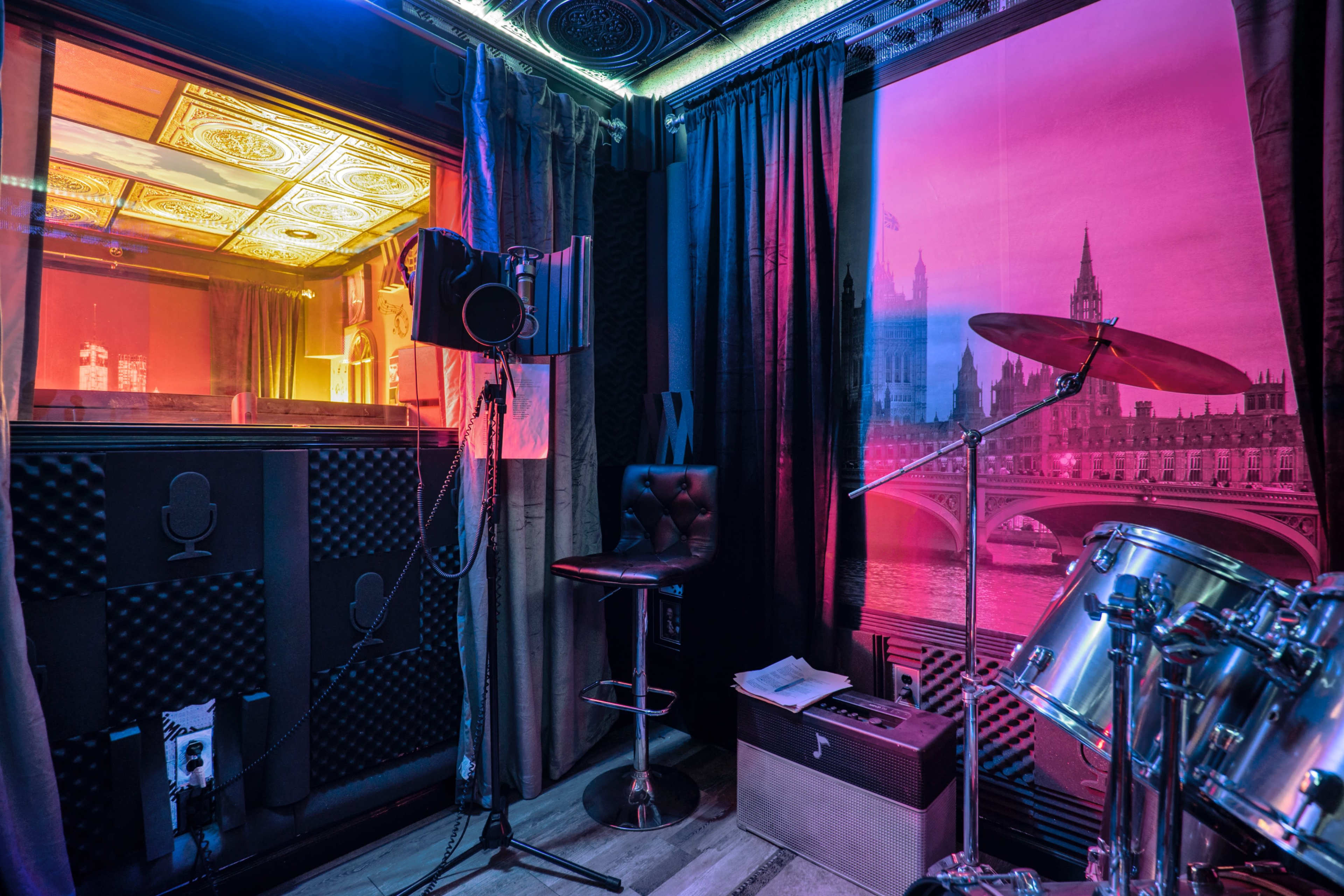 A small recording studio featuring a microphone on a stand, a drum set, and a visually striking backdrop of a cityscape.