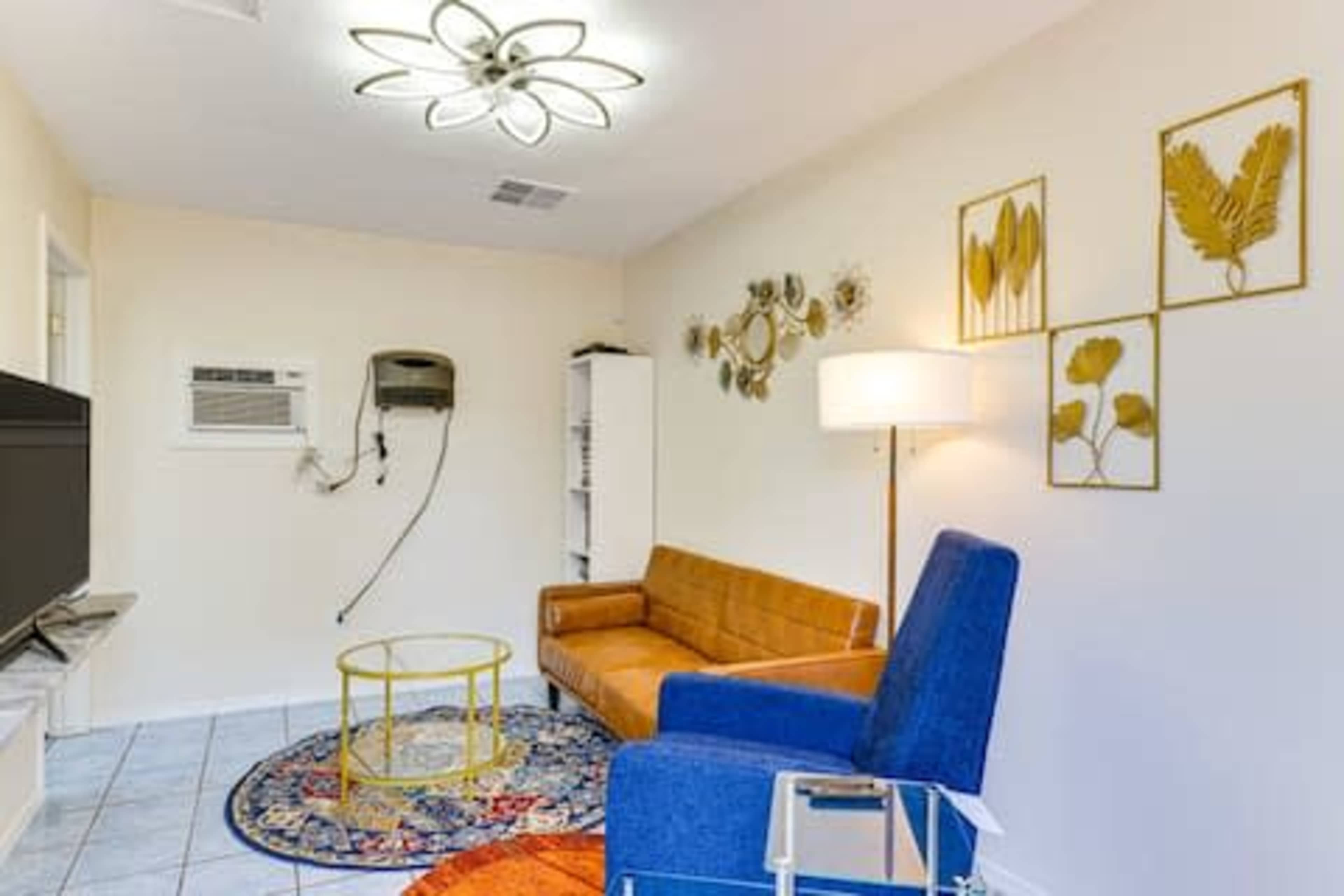 The image shows a small living room with a brown sofa, a blue chair, a round coffee table, and decorative wall art.