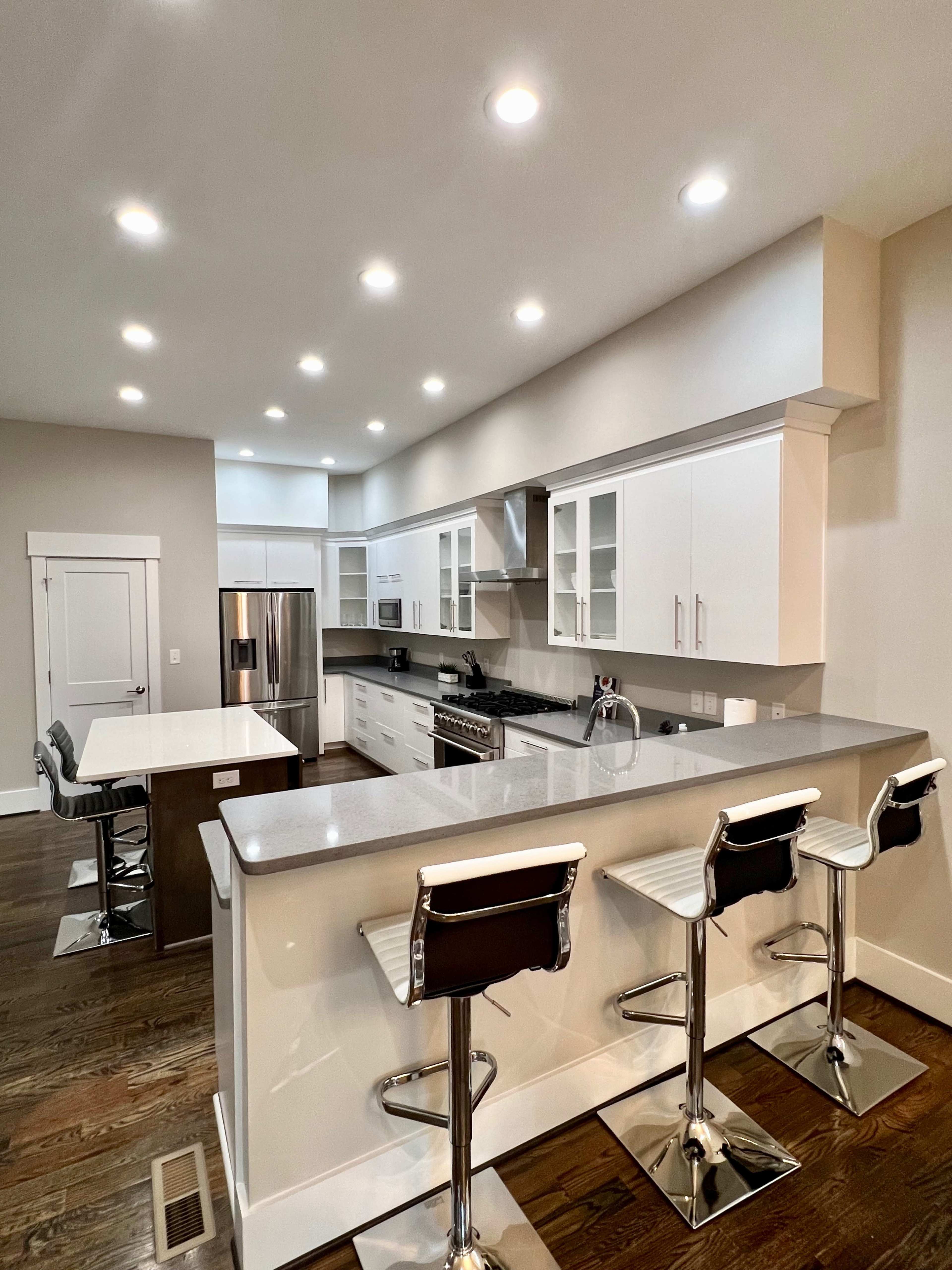 A modern kitchen with white cabinetry, stainless steel appliances, and a central island with four bar stools.
