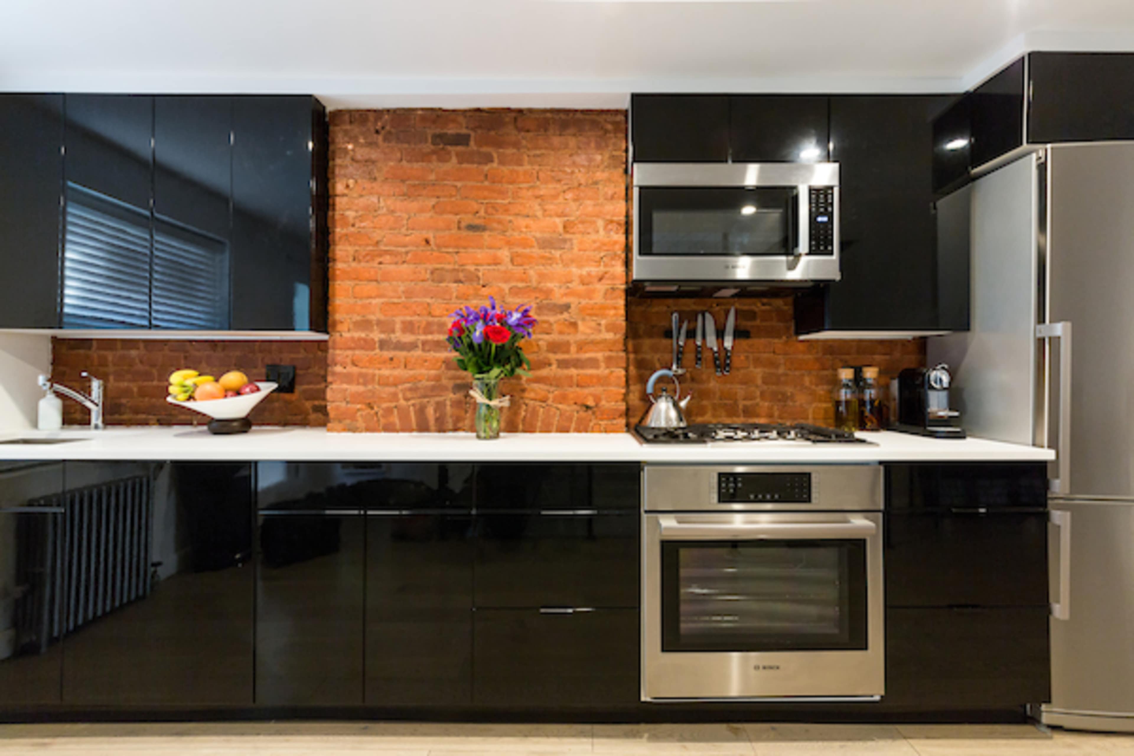 The kitchen features a modern design with black cabinetry, a stainless steel microwave and oven, and exposed brick walls.