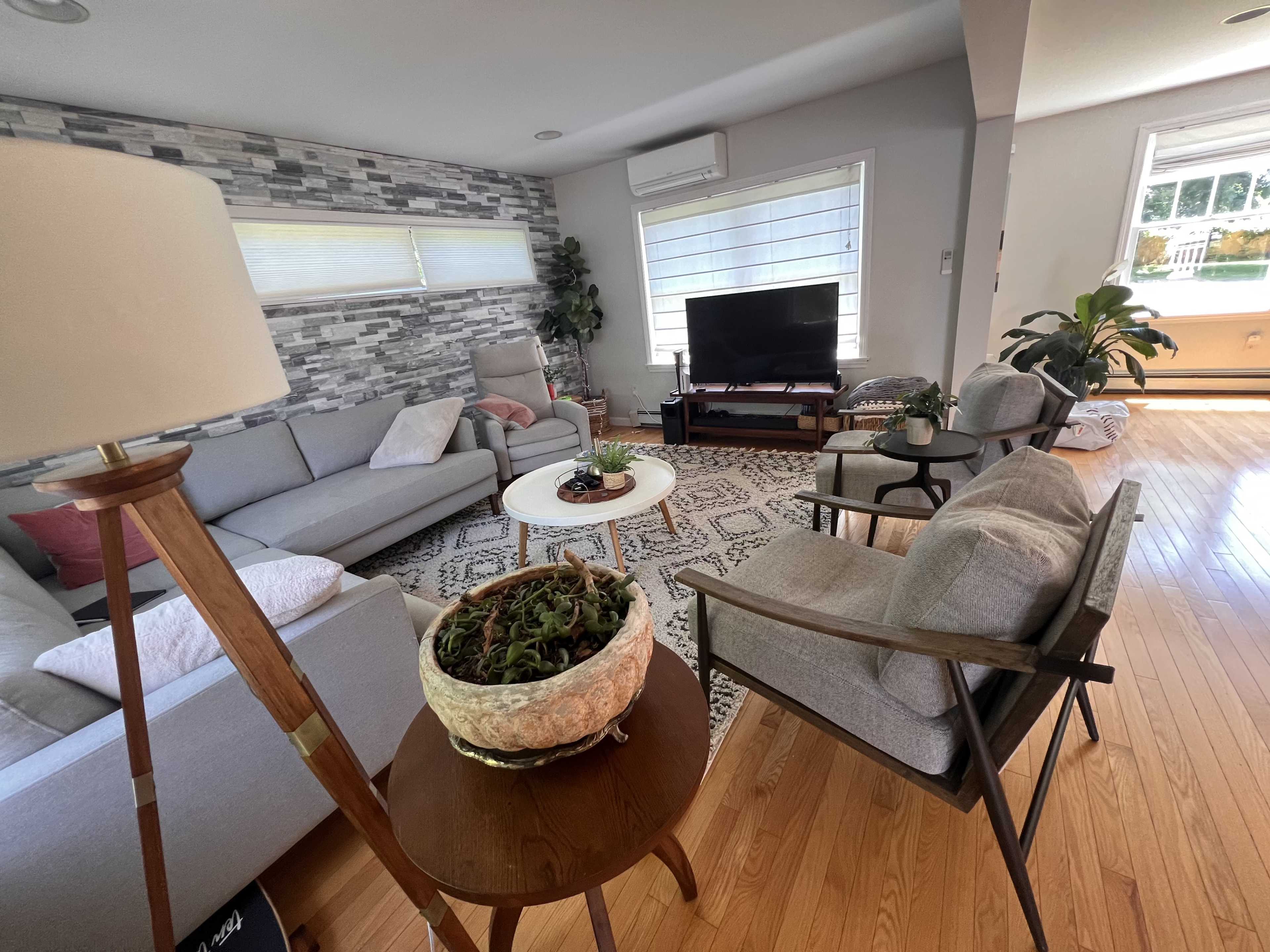 A cozy living room with a sectional sofa, a TV stand, and various plants, arranged around a patterned rug on hardwood flooring.