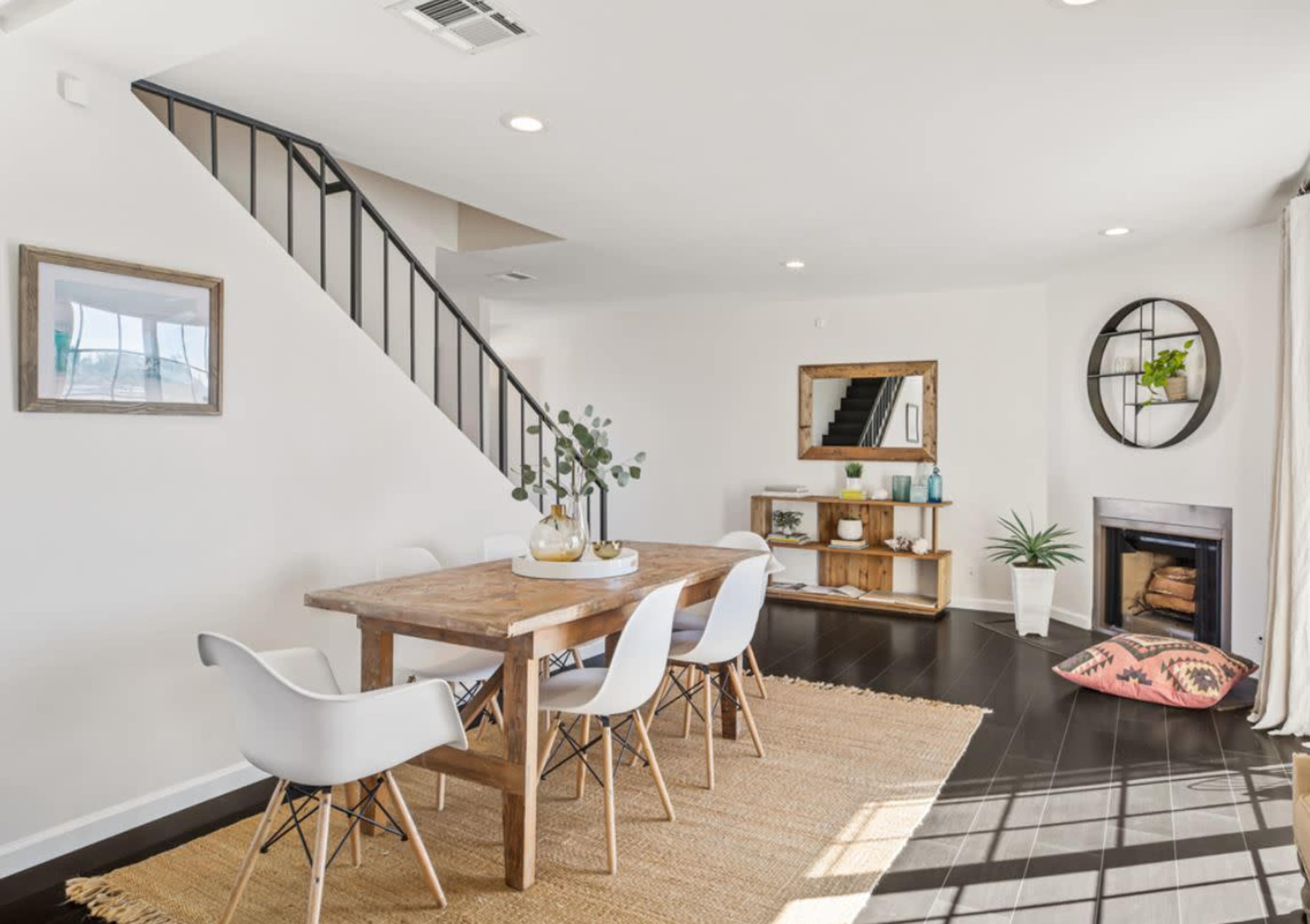 A modern dining area featuring a wooden table with white chairs, a decorative fireplace, and a staircase in the background.