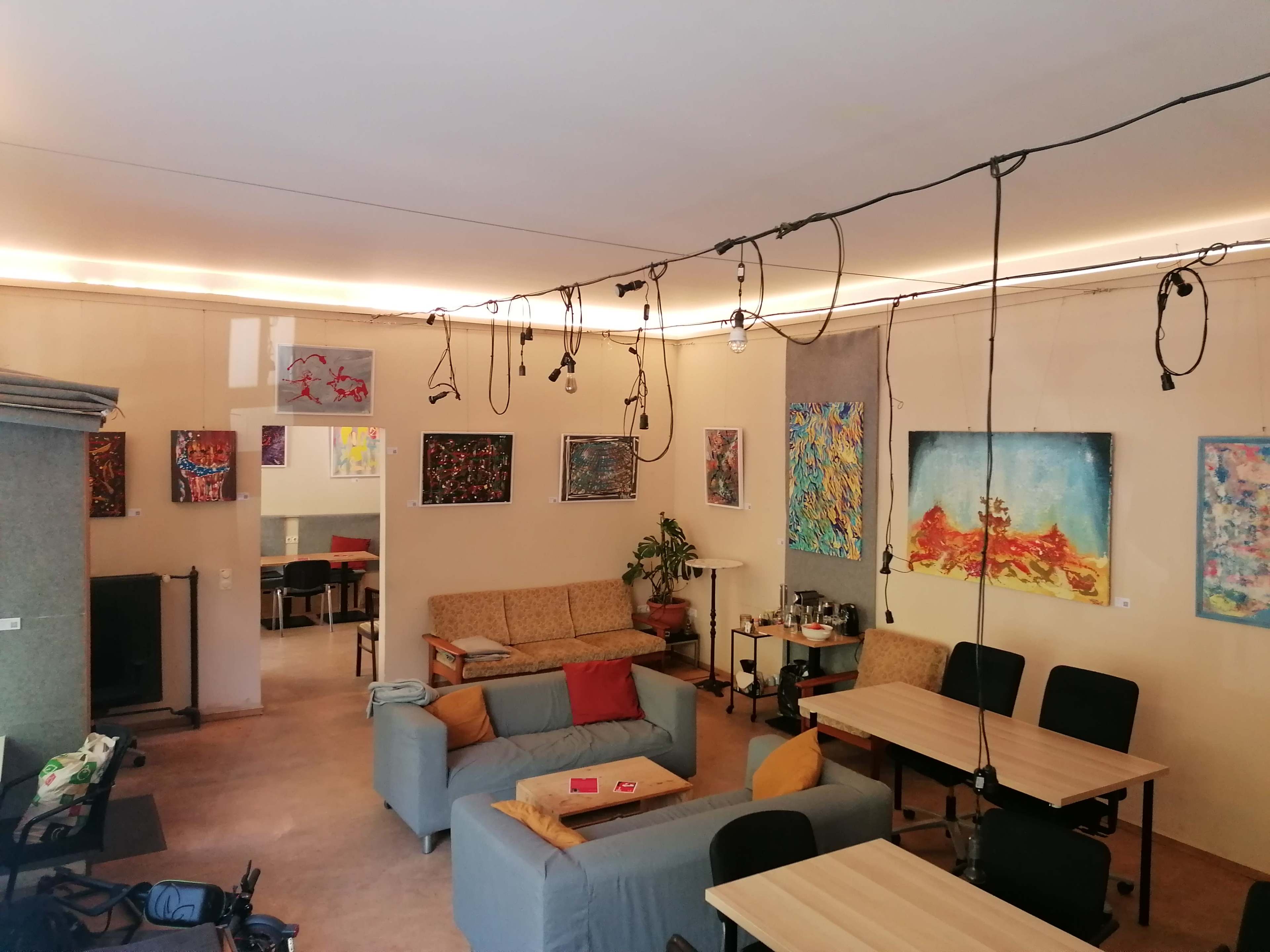 The image shows a large room featuring multiple artworks on the walls, various seating areas, and exposed wiring hanging from the ceiling.