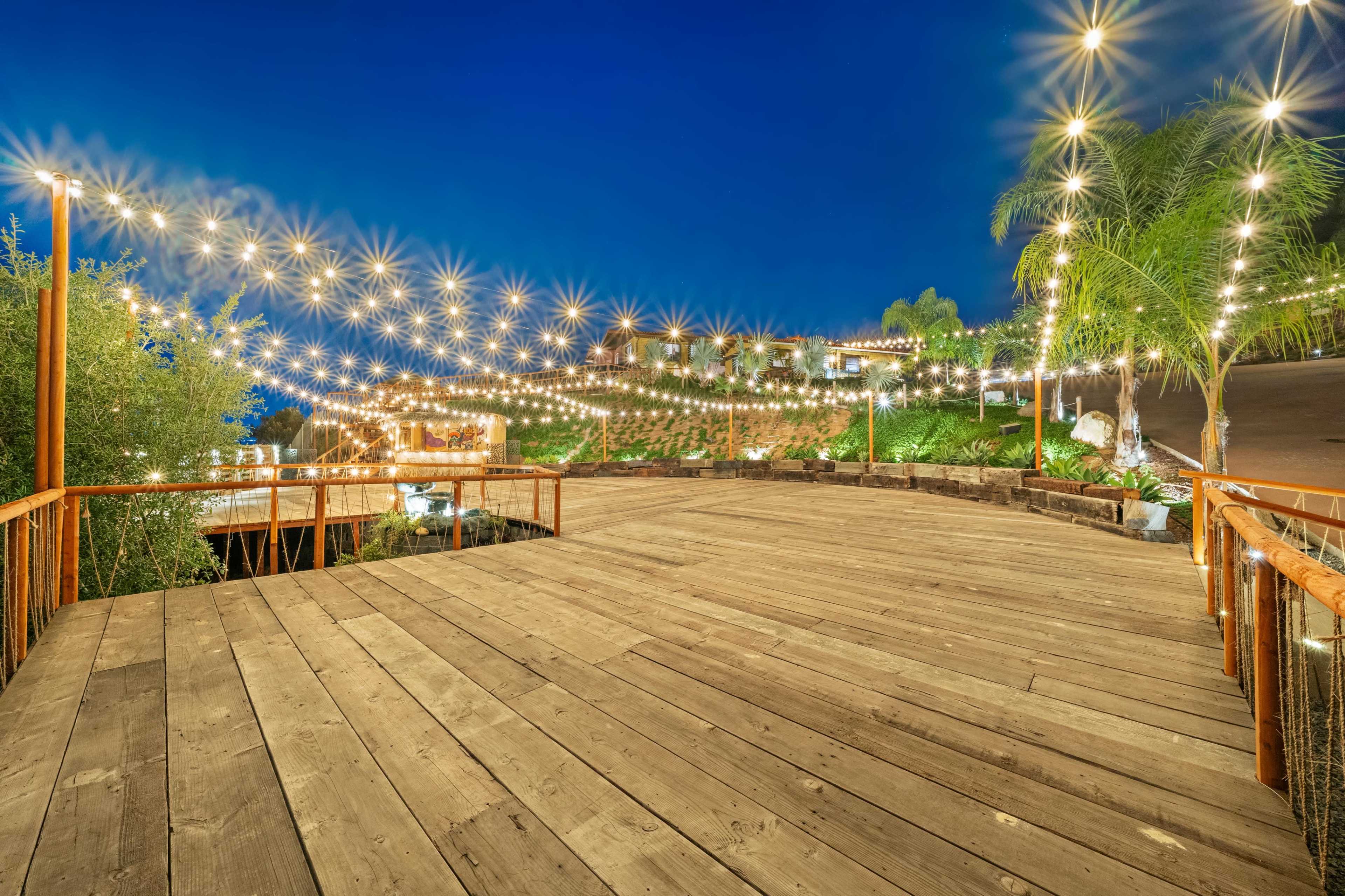 The image shows a wooden deck illuminated by string lights against a twilight sky, with a landscaped area in the background.