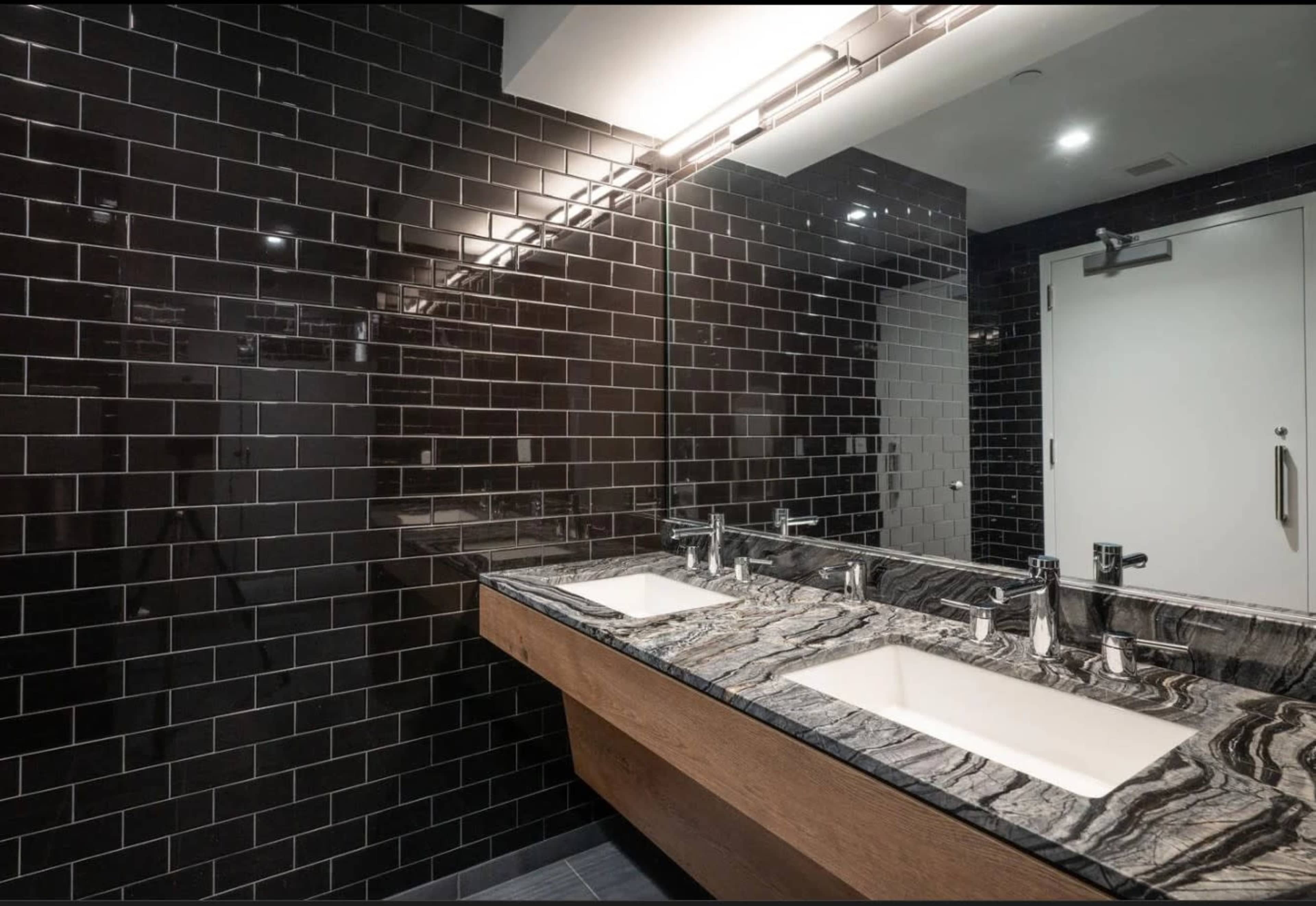 The image shows a modern bathroom with black tiled walls, a double sink vanity featuring a marble countertop, and contemporary fixtures.
