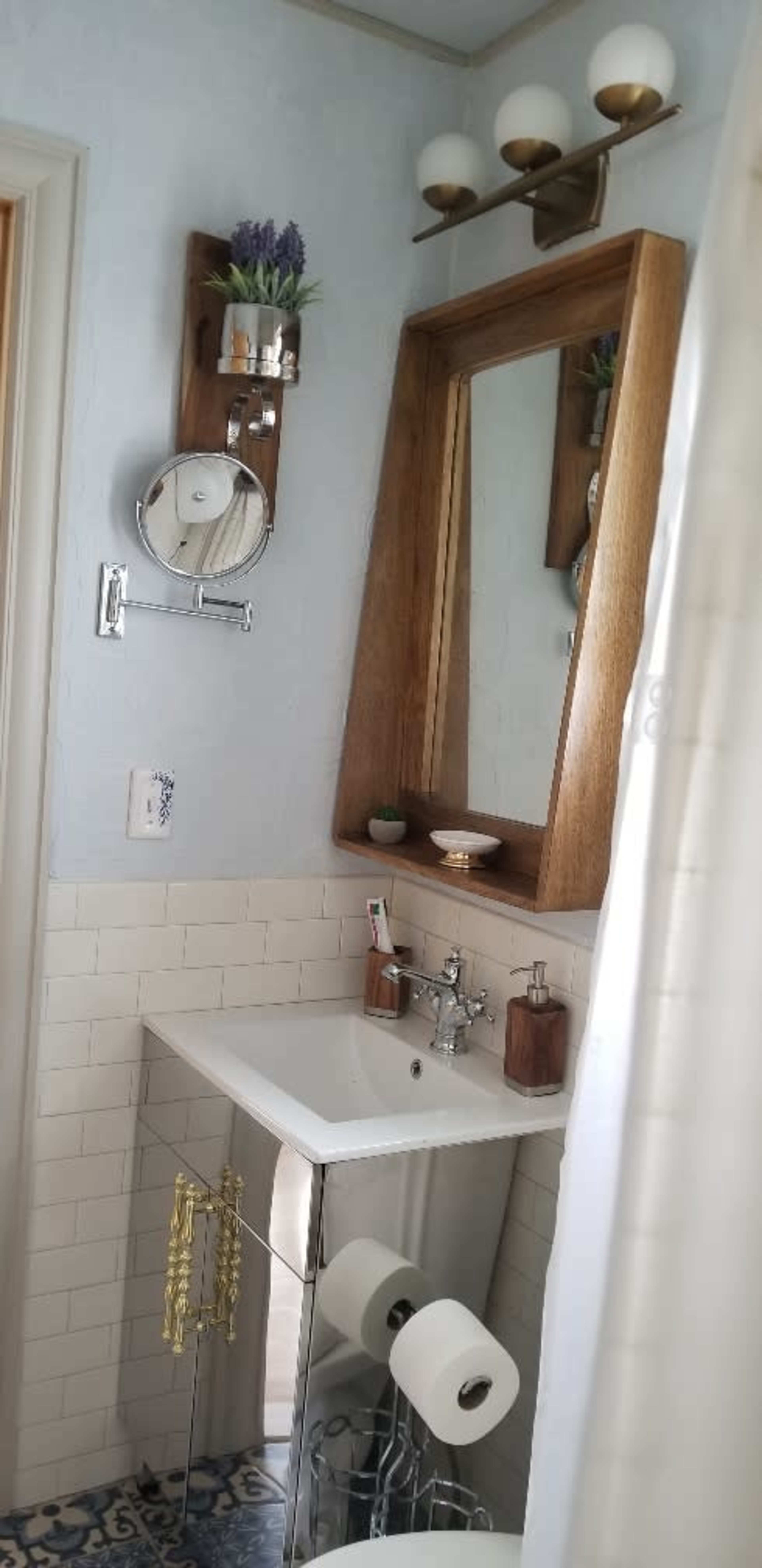 A compact bathroom featuring a floating sink with a wooden cabinet, a mirror with shelves, and a decorative towel holder.