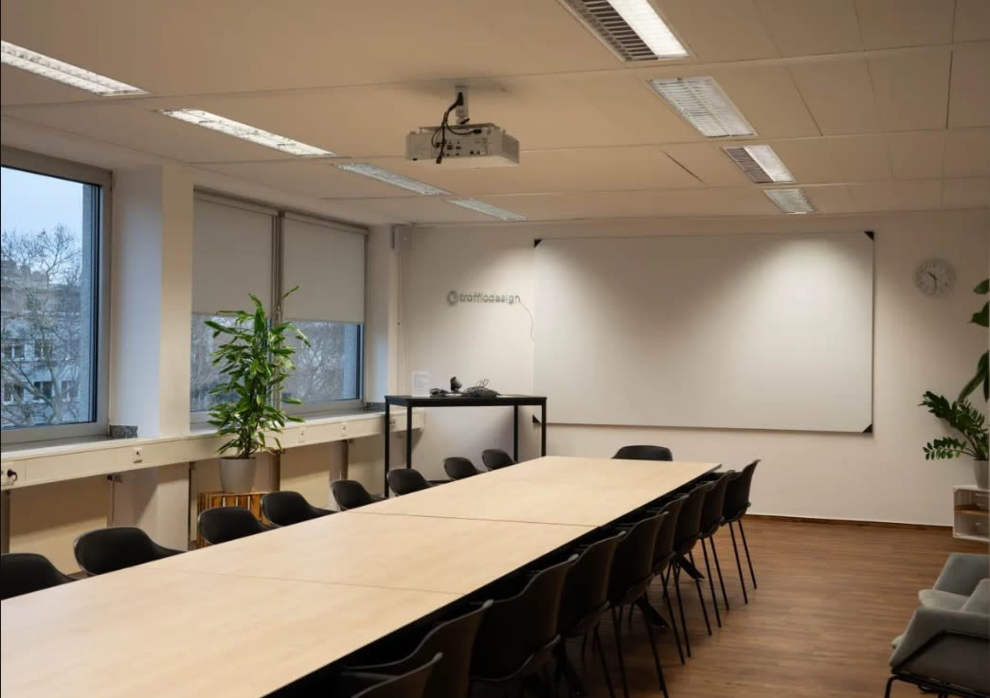 A conference room features a long table surrounded by black chairs, a projector on the ceiling, and a whiteboard at one end.