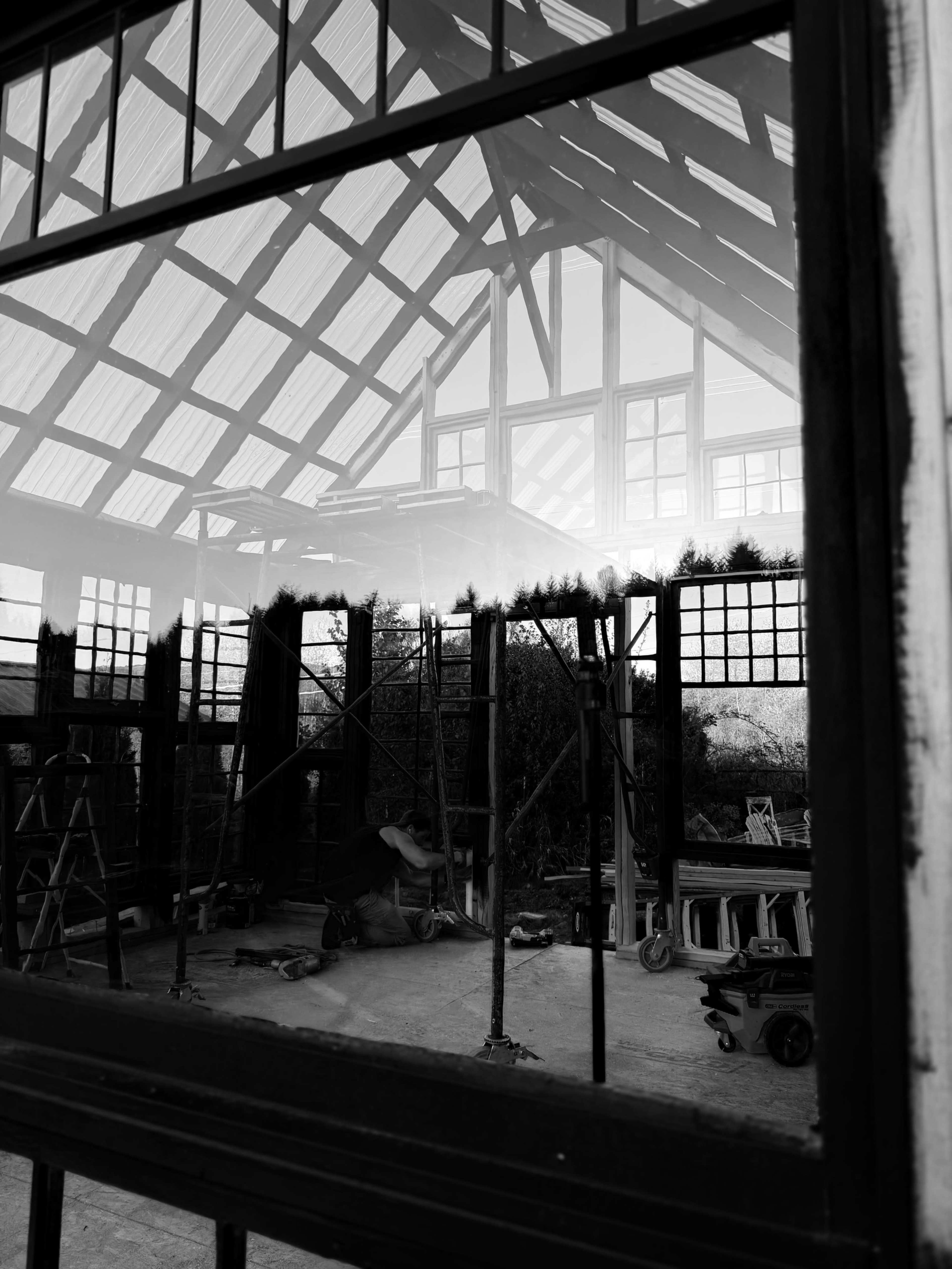 The image shows a black-and-white reflection of a construction site visible through a large window of a partially built structure.