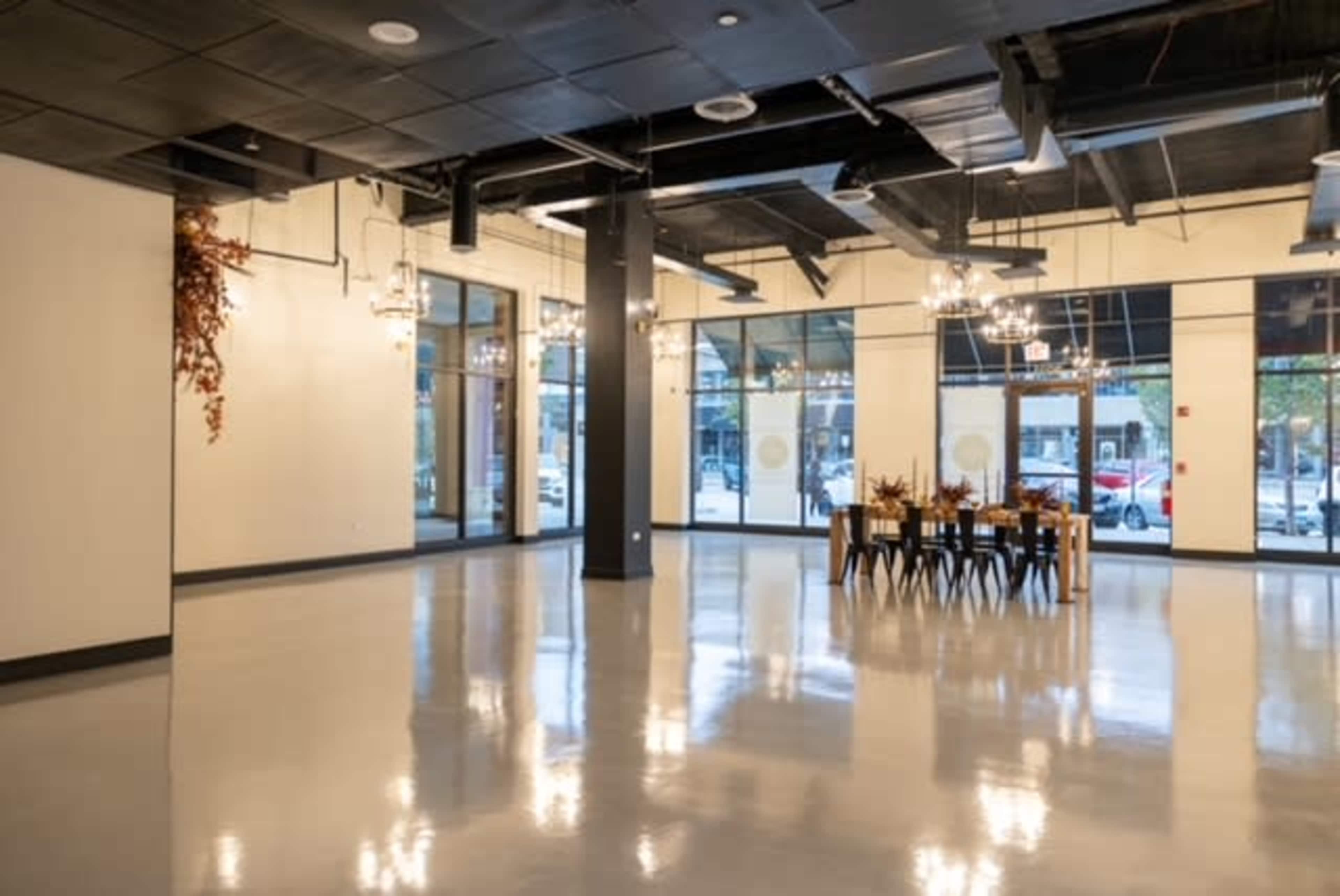 A spacious, empty room with polished flooring, large windows, and a long dining table set for guests.