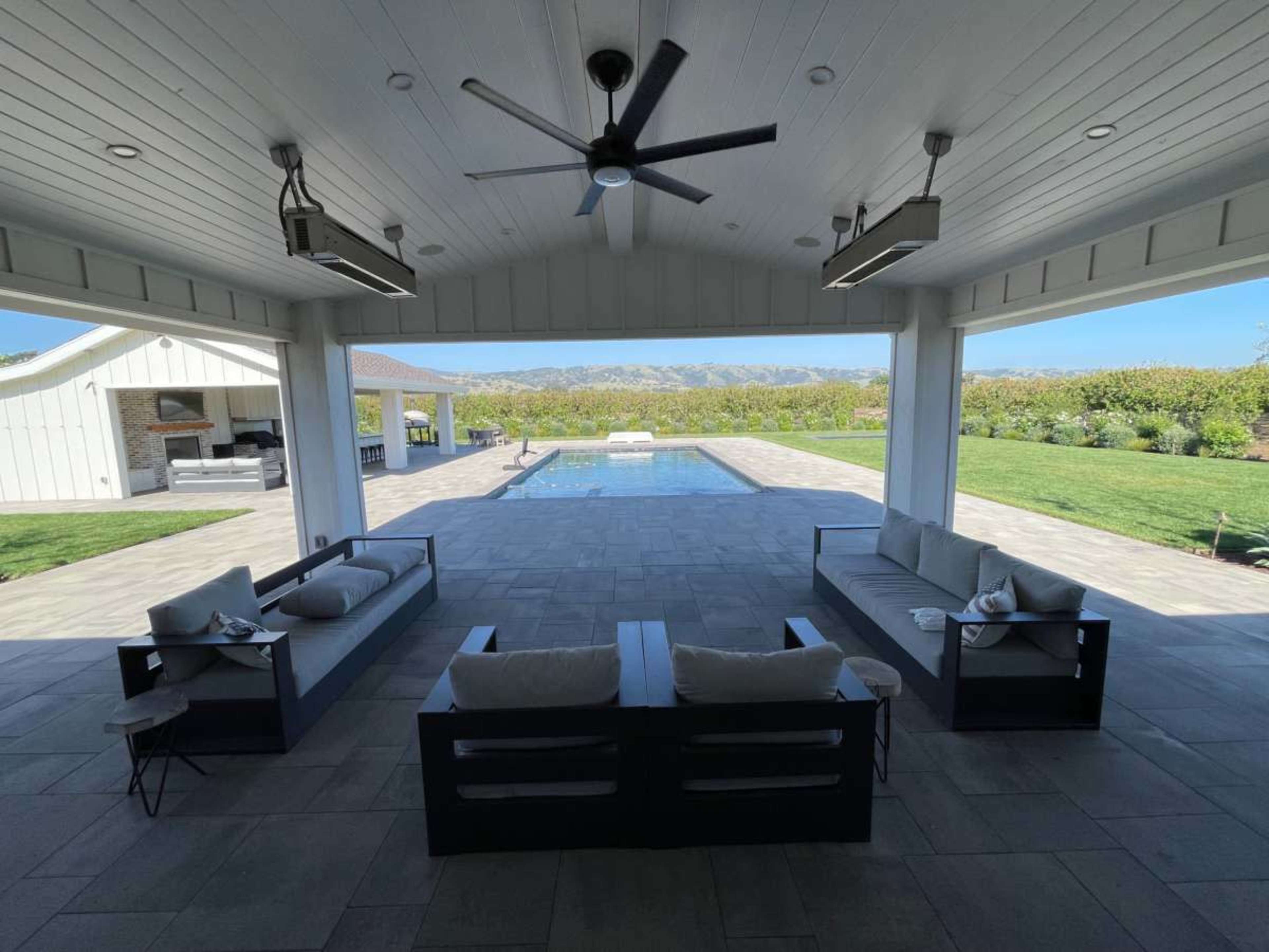 The image shows an outdoor patio area with modern seating arrangements facing a swimming pool and a vineyard in the background.