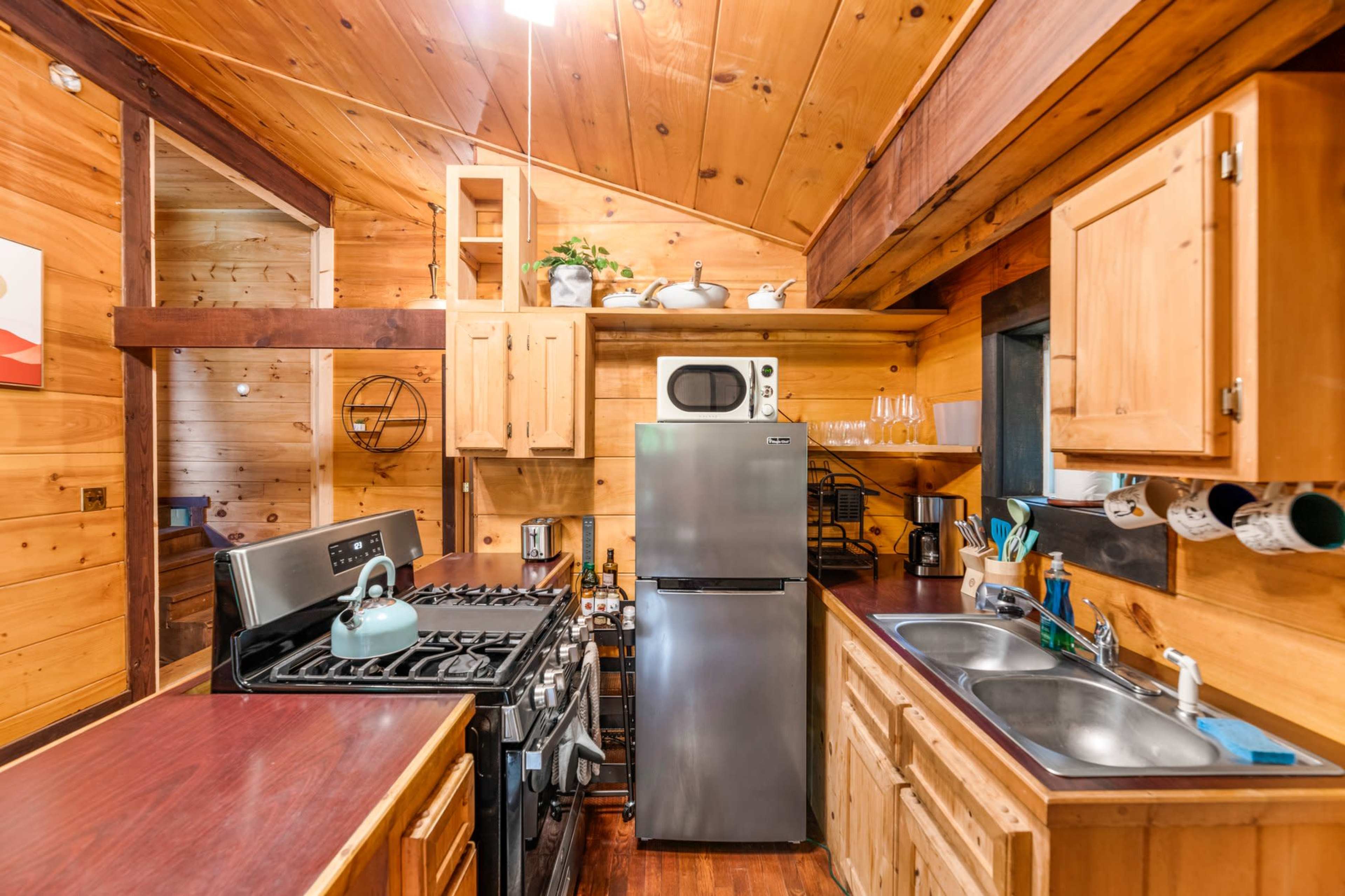 The kitchen features wooden walls, a gas stove, a silver refrigerator, and a double sink along with open shelving and various kitchen utensils.