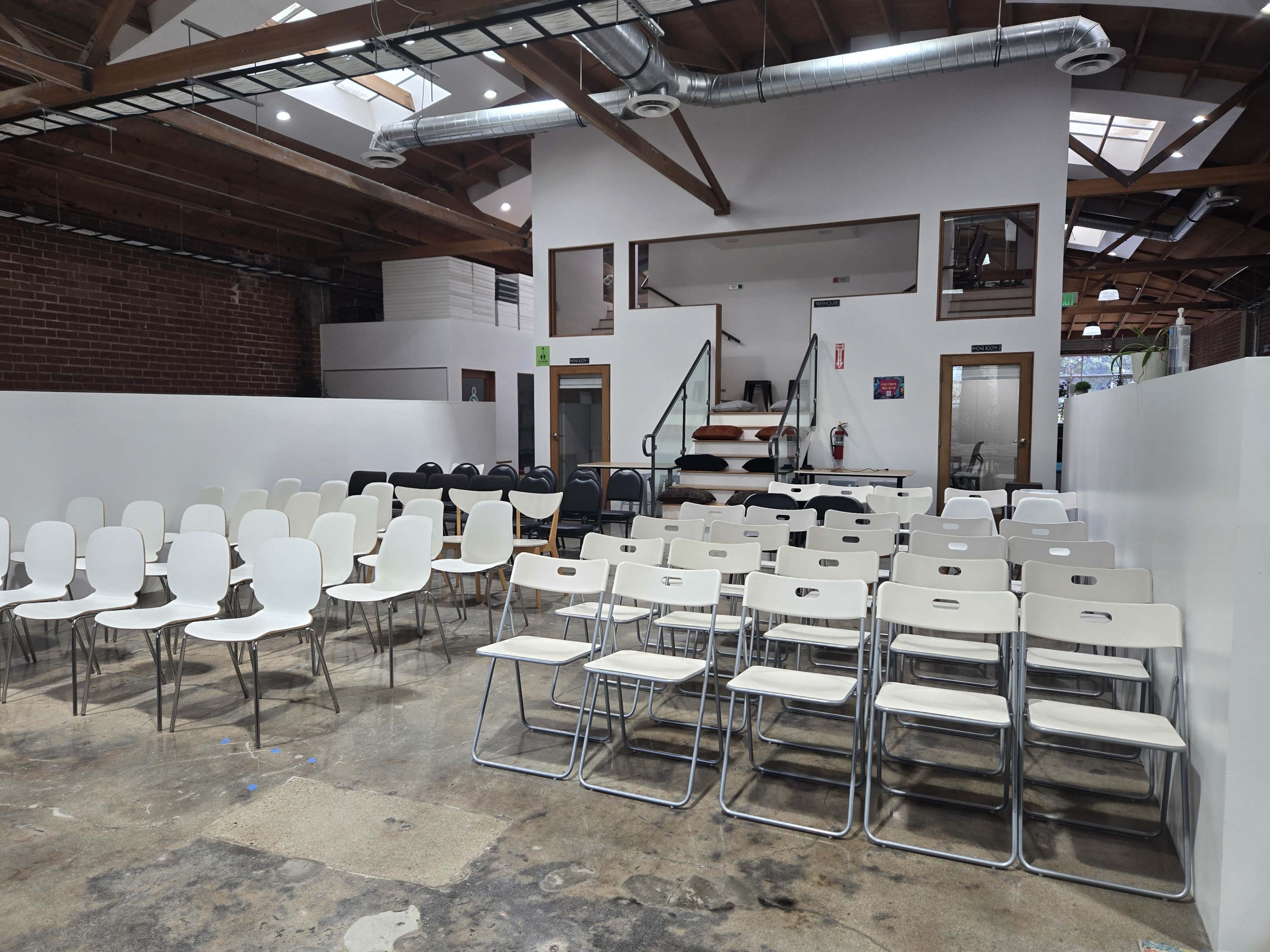 The image shows a spacious interior with a set of white and black folding chairs arranged facing a staircase and an upper level.