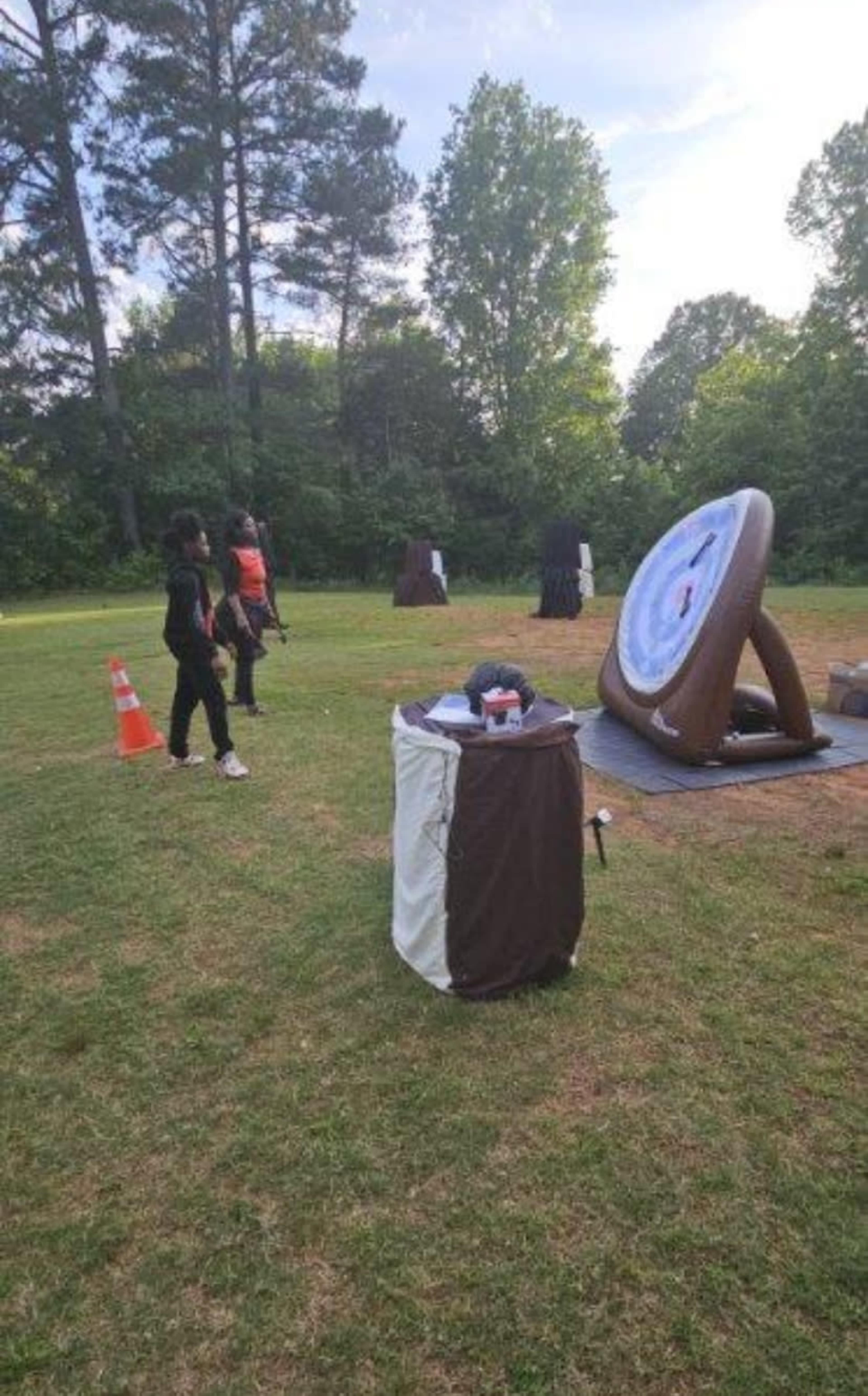 The image shows a grassy area with several archery targets set up, while individuals are positioned nearby.