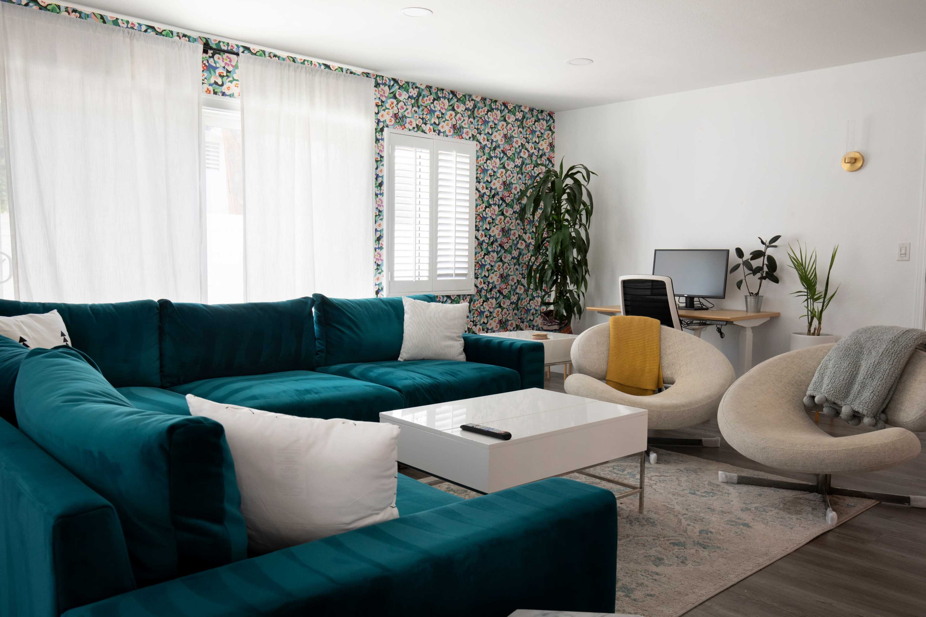 The image shows a modern living room with a teal sectional sofa, a white coffee table, a light-colored desk with a computer, and a decorative plant.