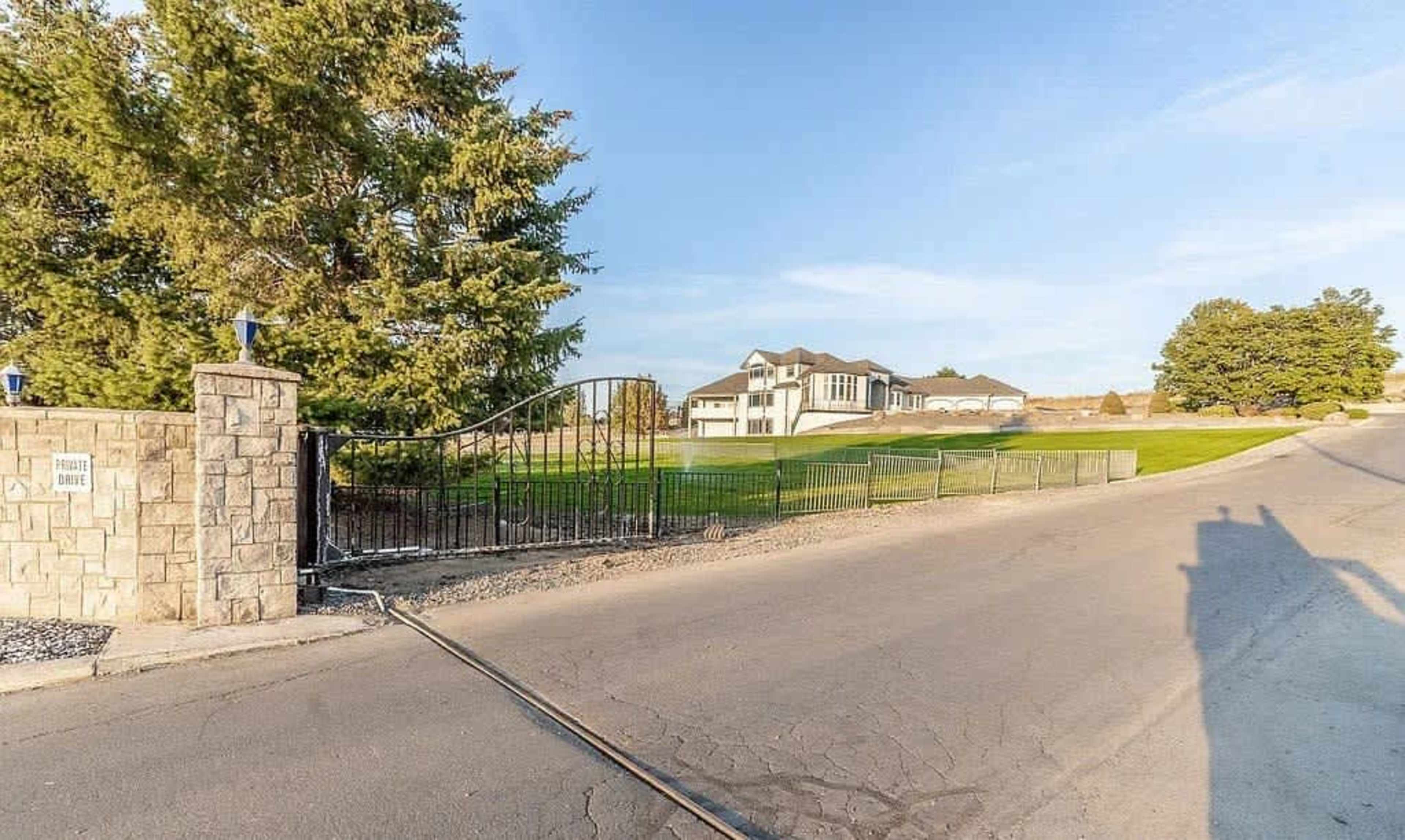 A large house is visible in the background behind a gated entrance along a paved road.
