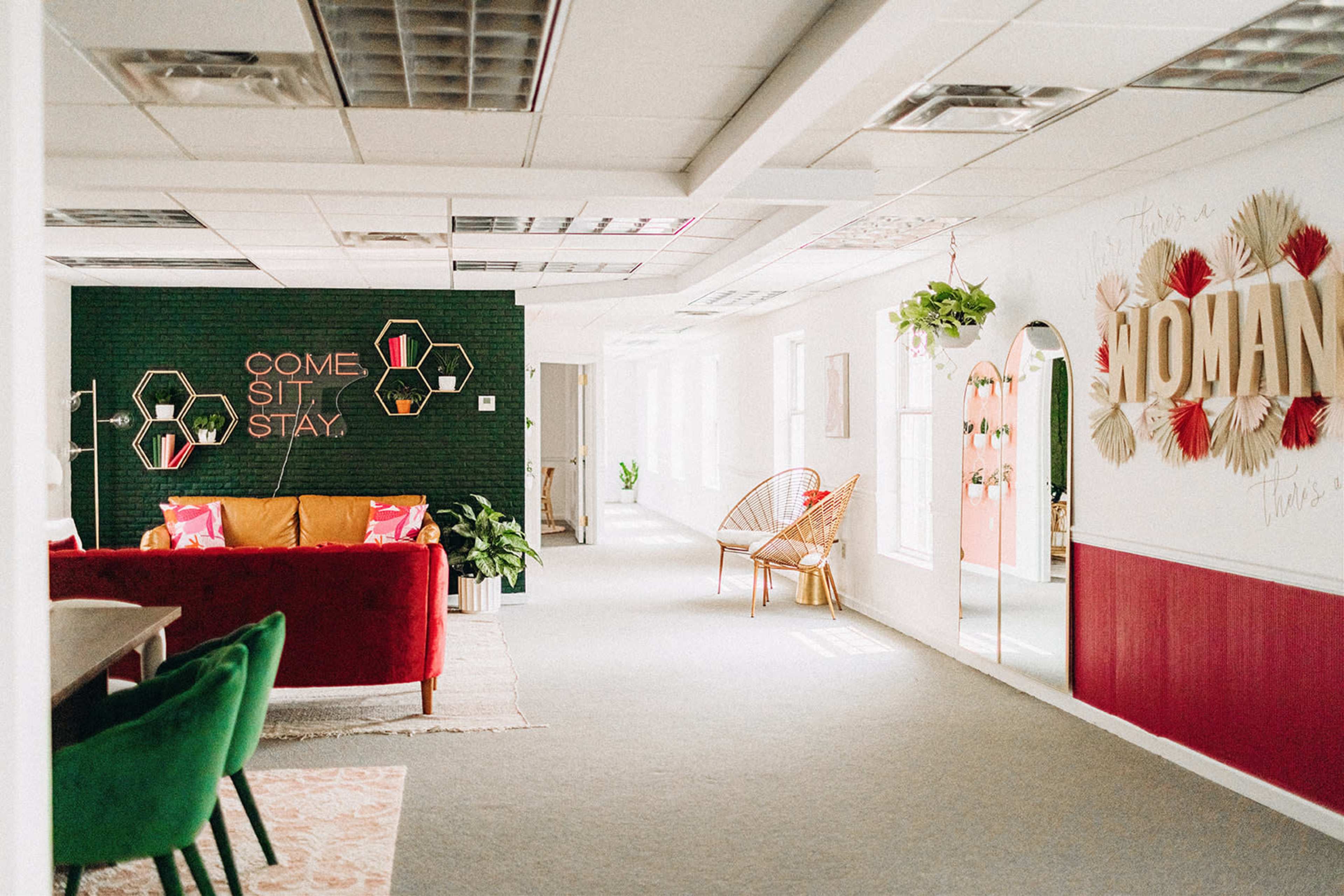 A modern office space with a bright red sofa, green accents, and decorative wall art, including a large sign that reads "WOMAN."