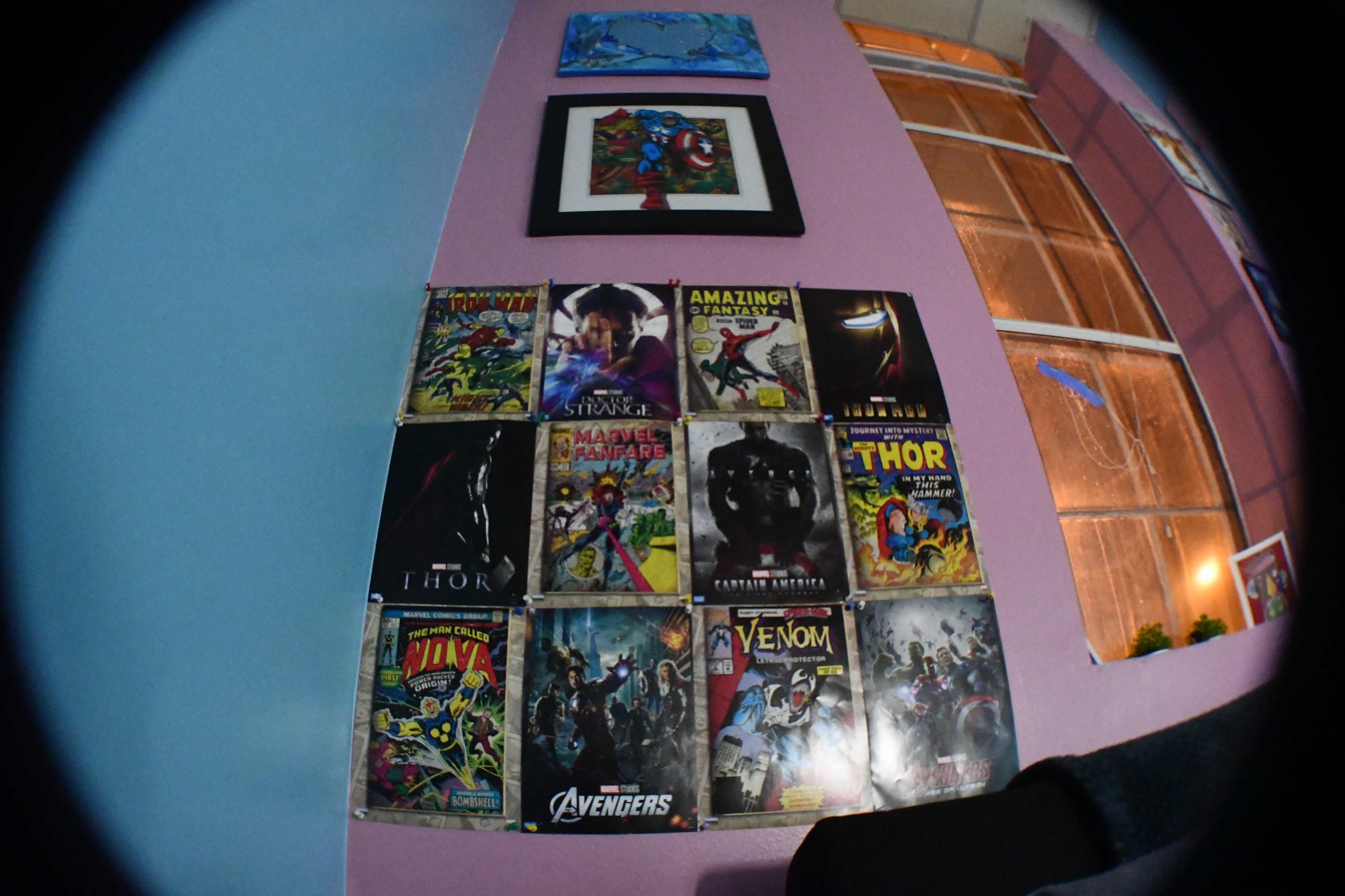 A wall decorated with various comic book covers arranged in a grid pattern, featuring characters like Thor, Venom, and the Avengers.