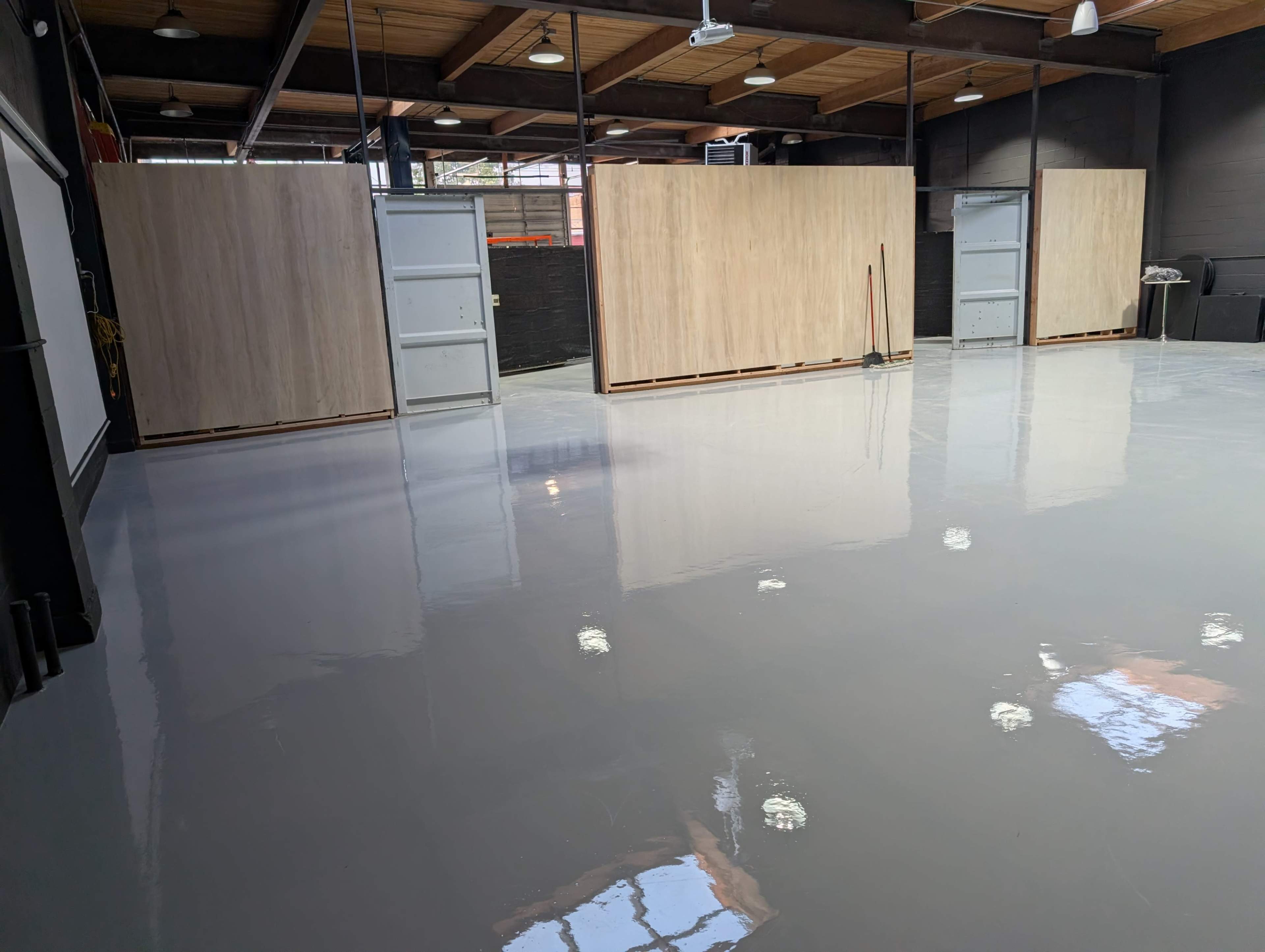 The image shows a large, open industrial space with a shiny gray floor, wooden partition walls, and overhead lighting.