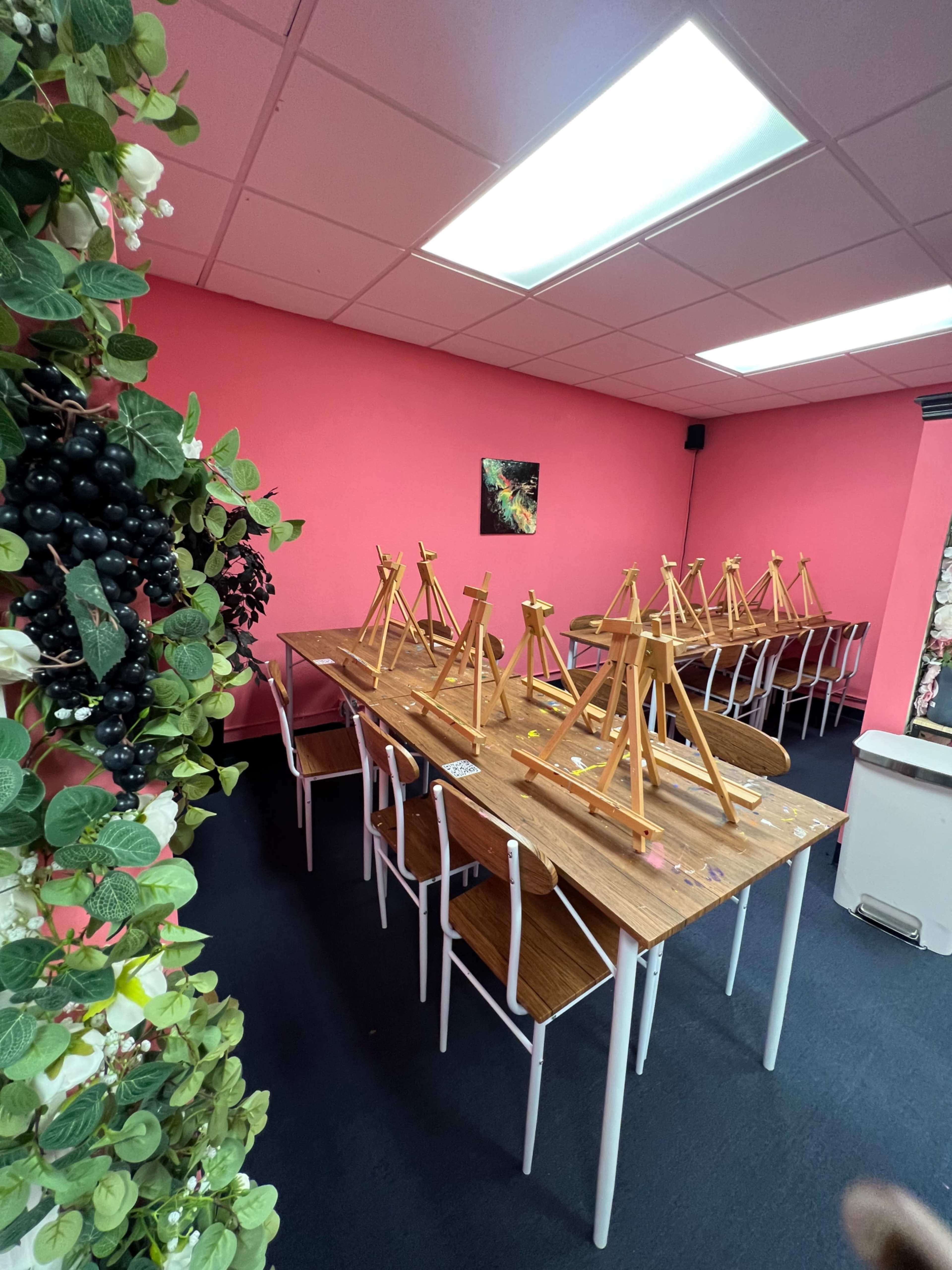A brightly colored room with a long table set up with multiple wooden easels arranged for an art class.