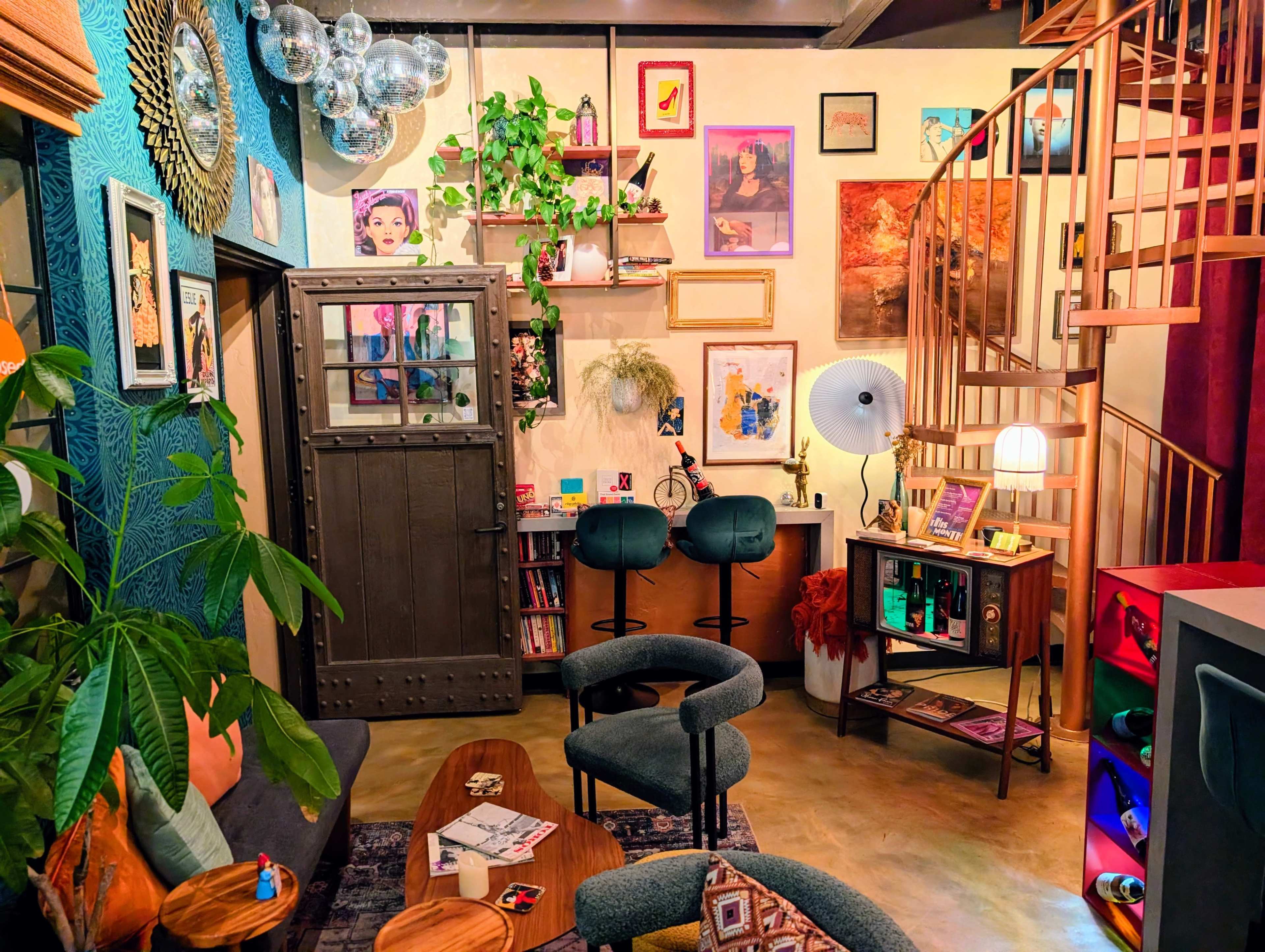 The image depicts a cozy, eclectic living space featuring colorful artwork, plants, and a spiral staircase.