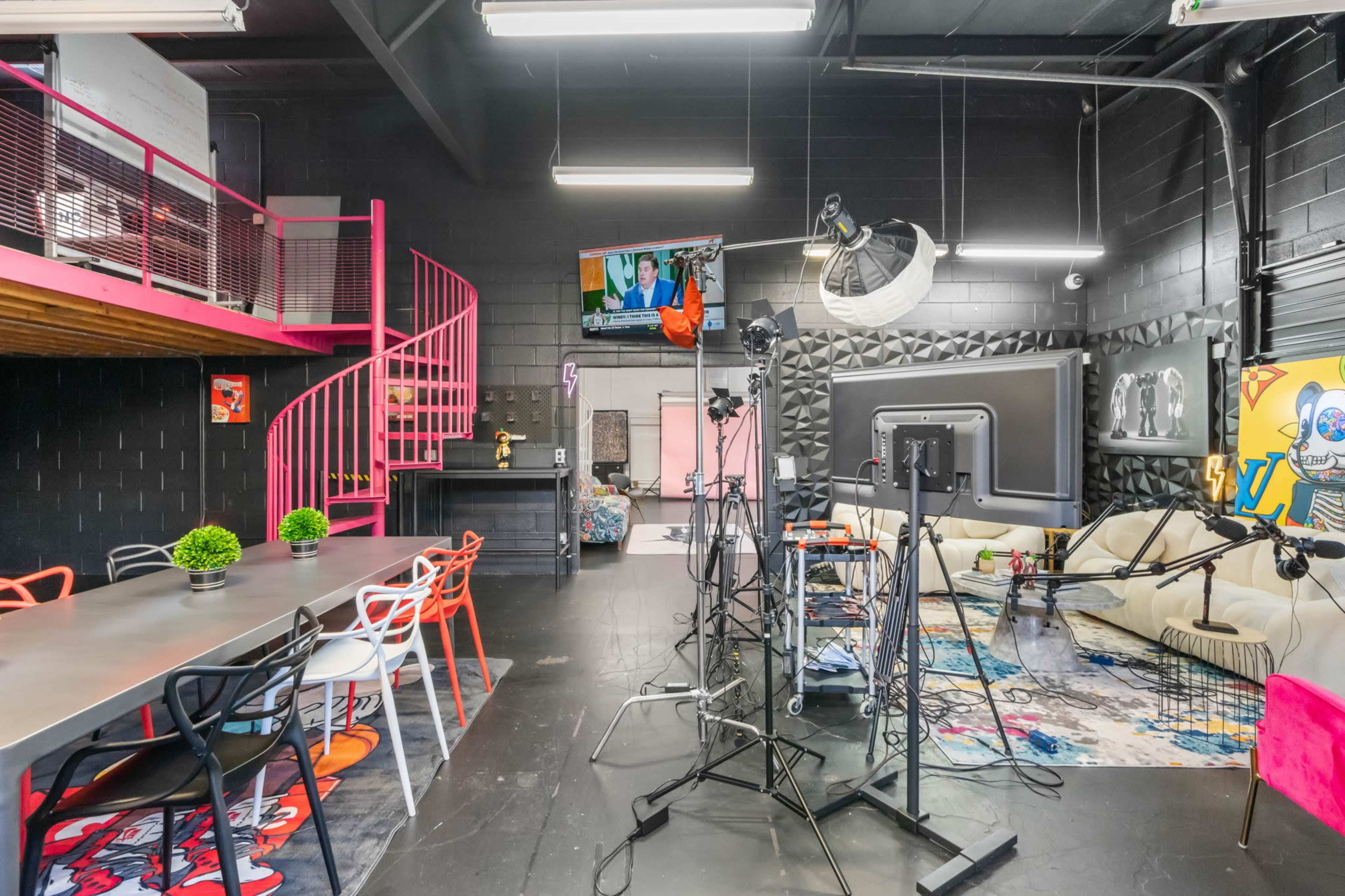 A modern studio space featuring a spiral staircase, a large screen on the wall, and various equipment set up for filming or recording.