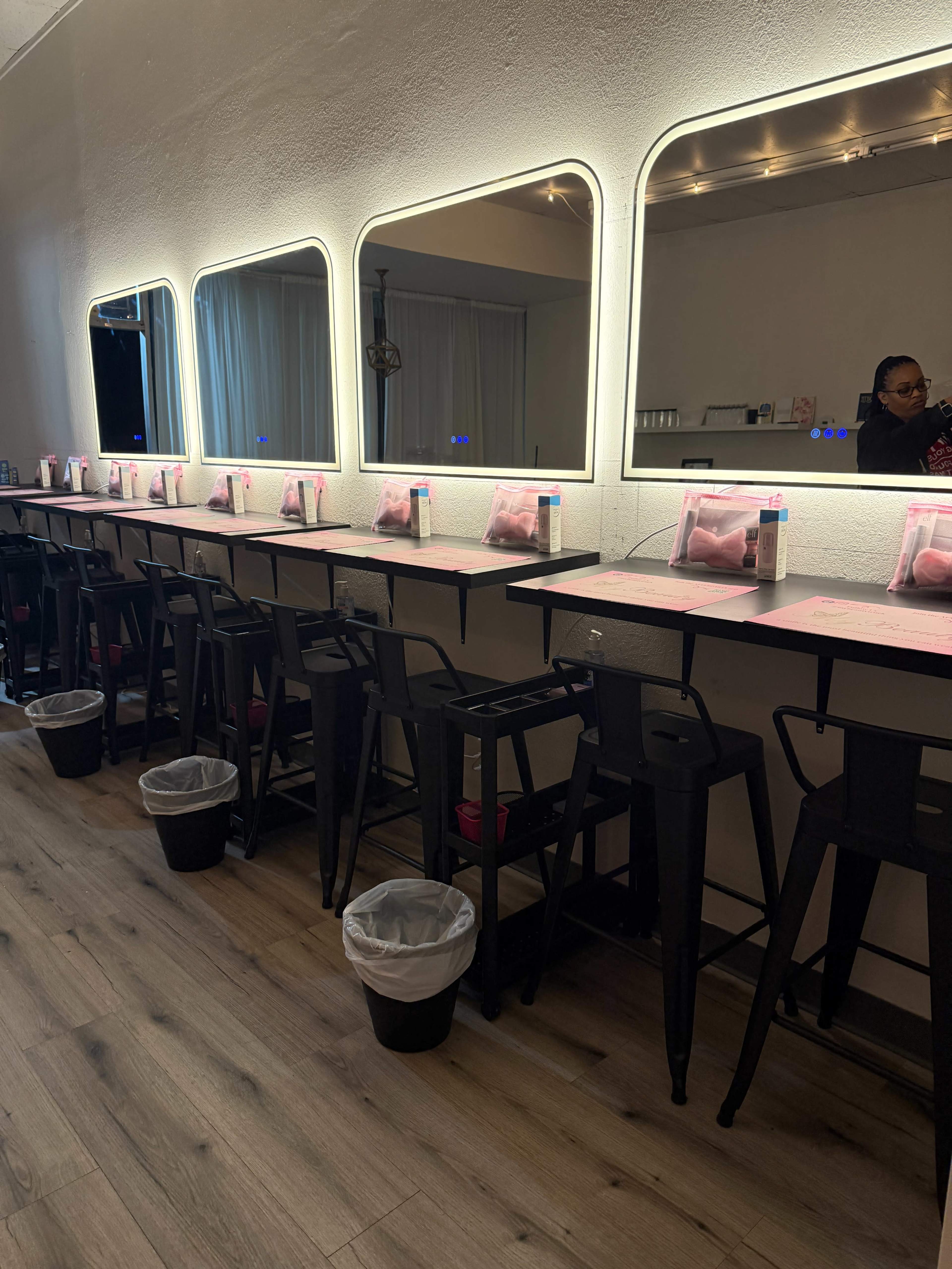 The image shows a brightly lit interior of a cafe or restaurant with several high tables and stools, illuminated mirrors, and wall-mounted trash bins at the base of each table.
