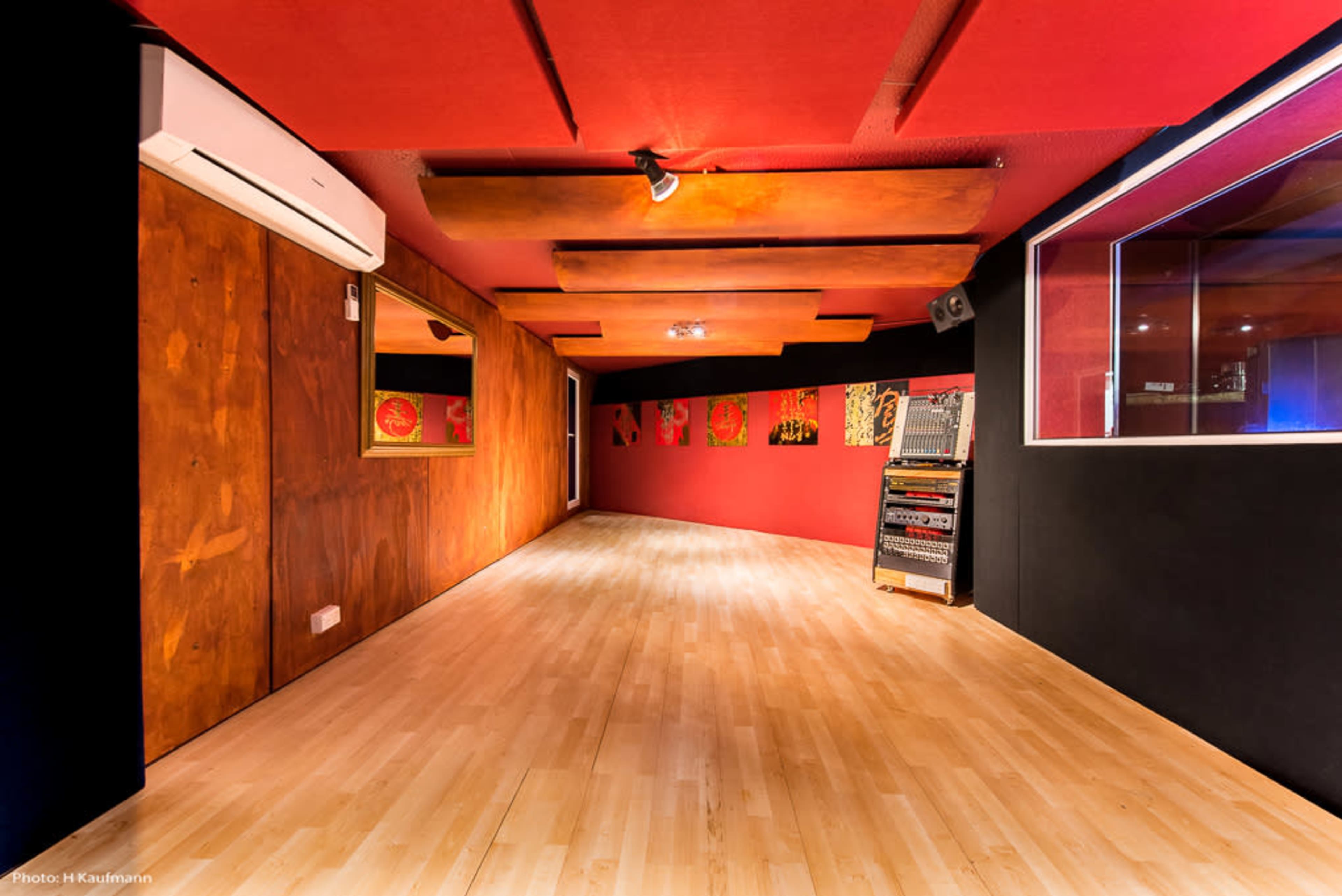 The image shows a music recording studio with wooden flooring, red walls, and soundproofing features.