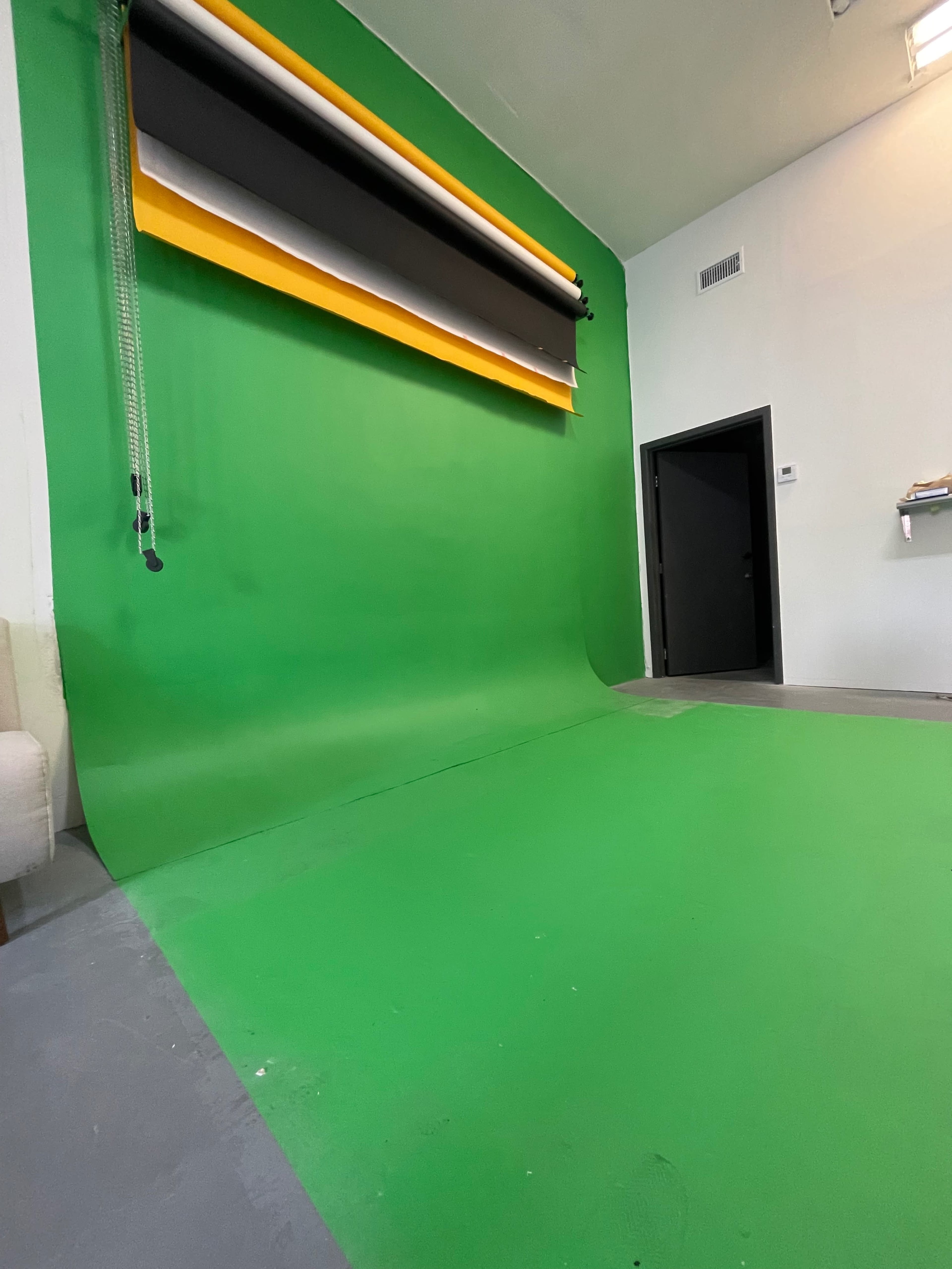 A photography studio with a green screen backdrop and a door in an adjacent wall.