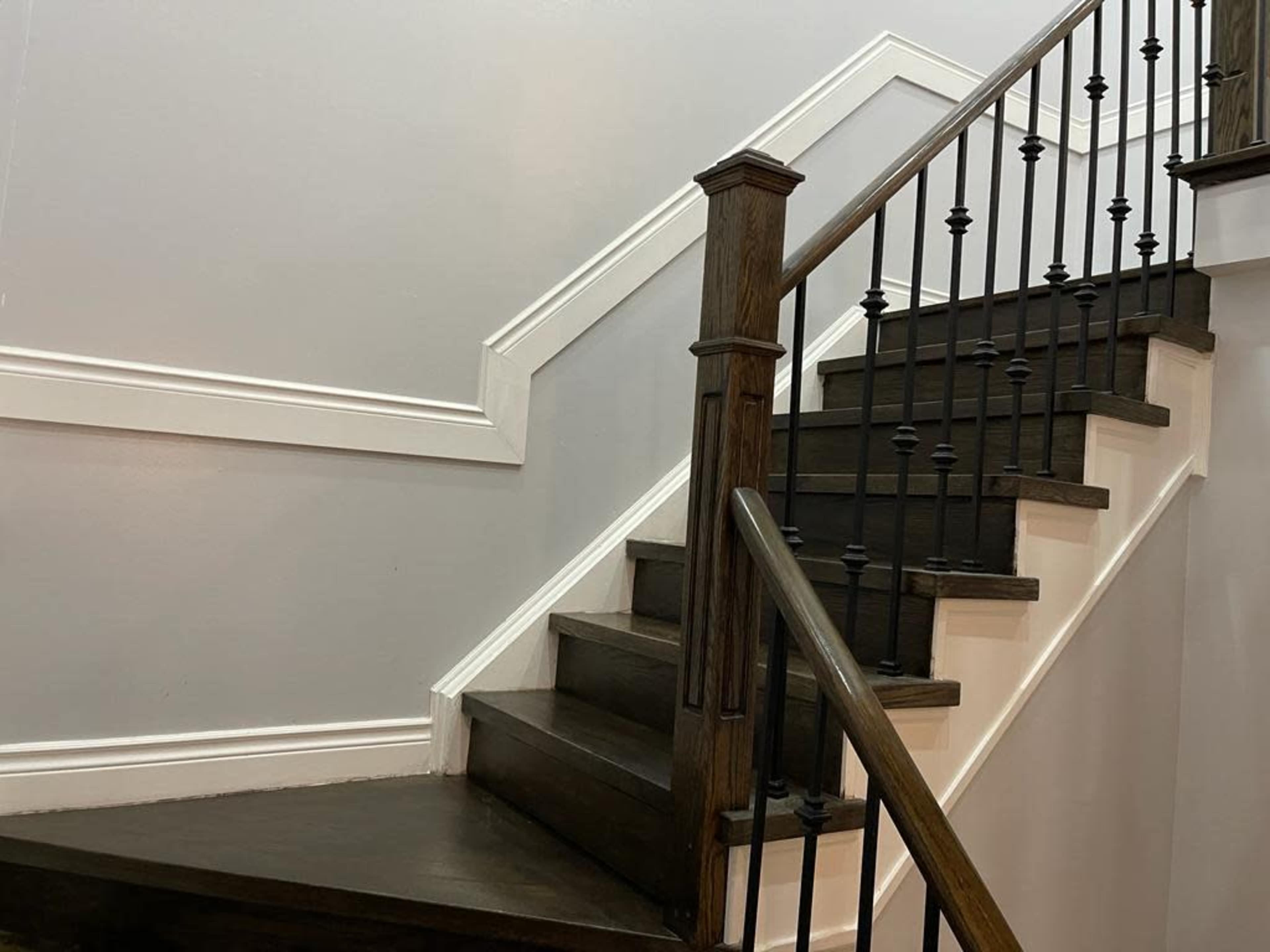 A wooden staircase with metal balusters and a grey wall, featuring white trim.